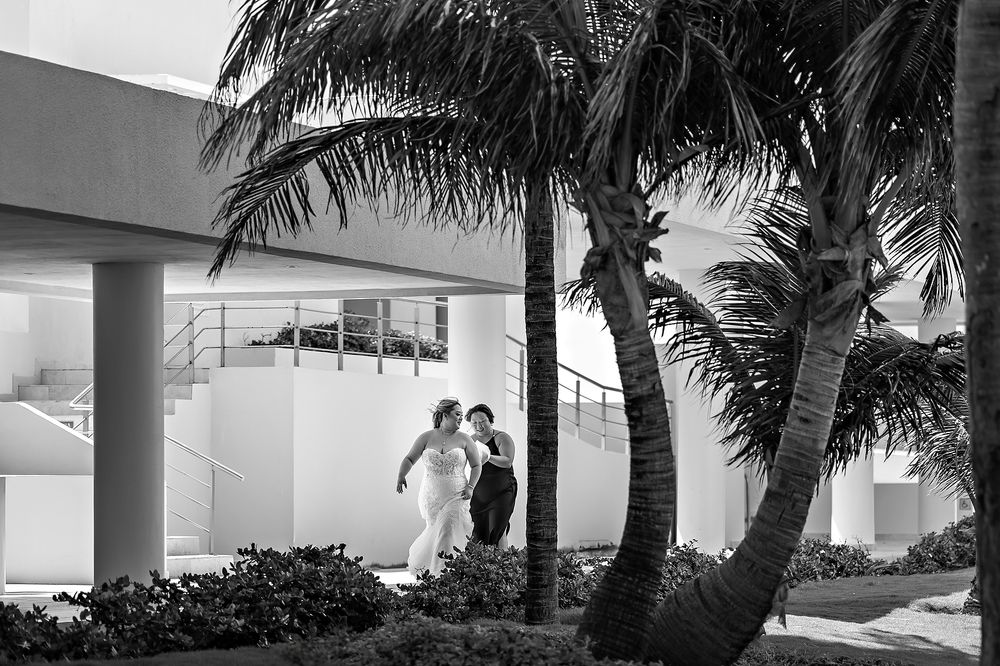 A romantic couple embraces on a walkway between modern white architecture and swaying palm trees on a breezy day.