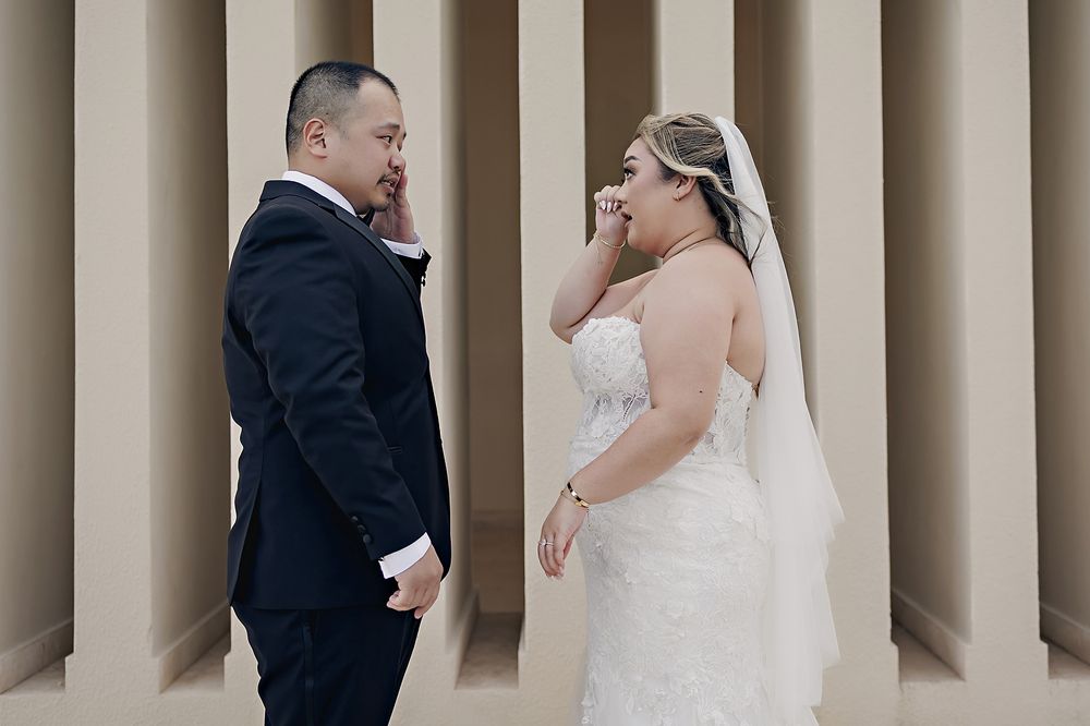 A bride and groom share a candid moment of laughter together against a beige columned wall during their wedding at Hyatt Ziva Cancun.