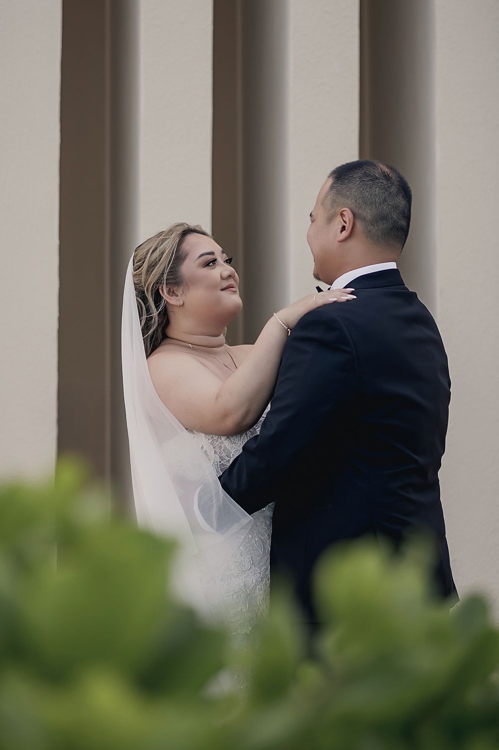 A bride in a white gown and groom in a black suit embrace intimately against architectural columns during their wedding at Hyatt Ziva Cancun