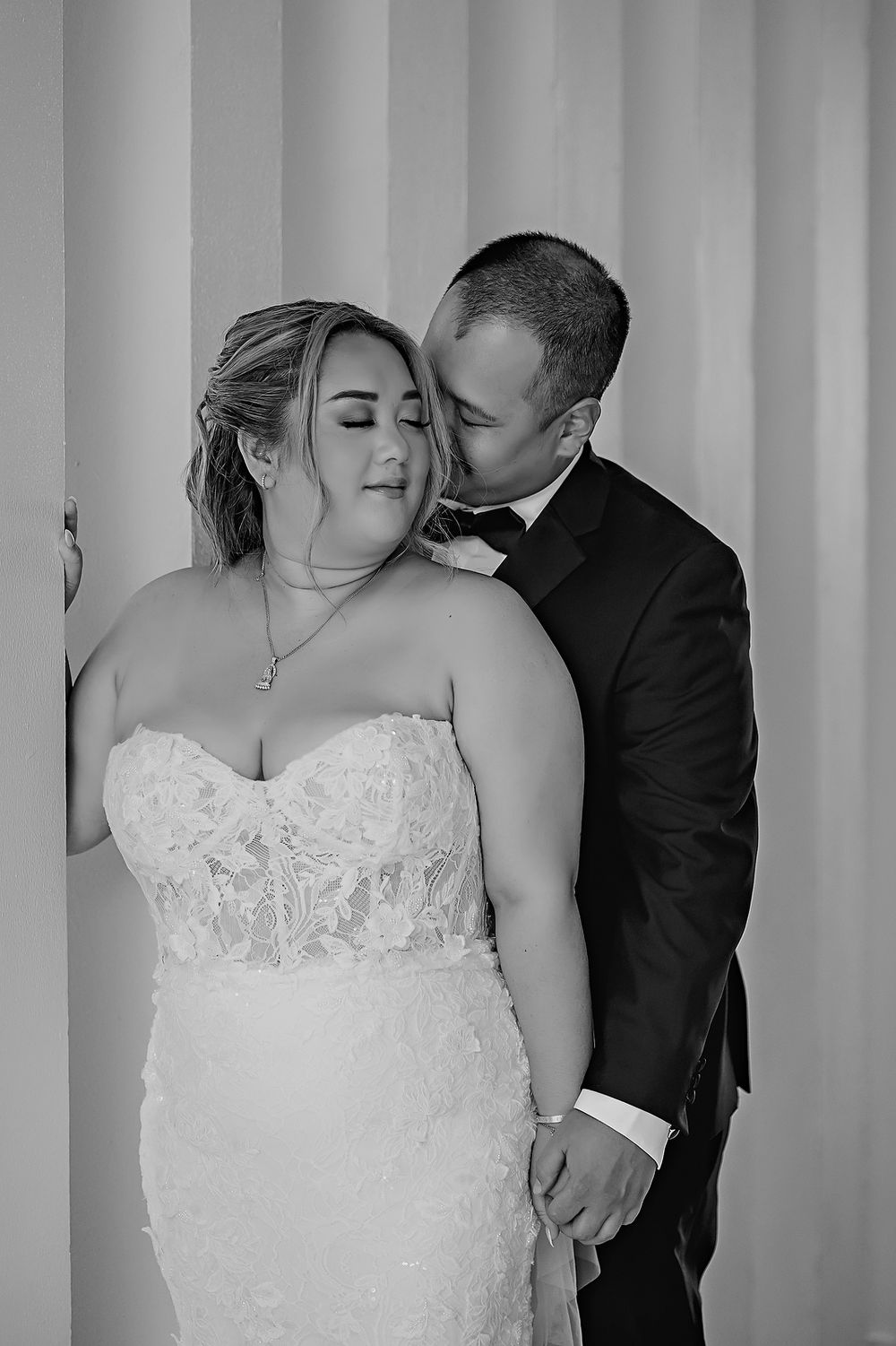 Black and white romantic wedding portraits show a bride in a lace dress embracing with her groom.