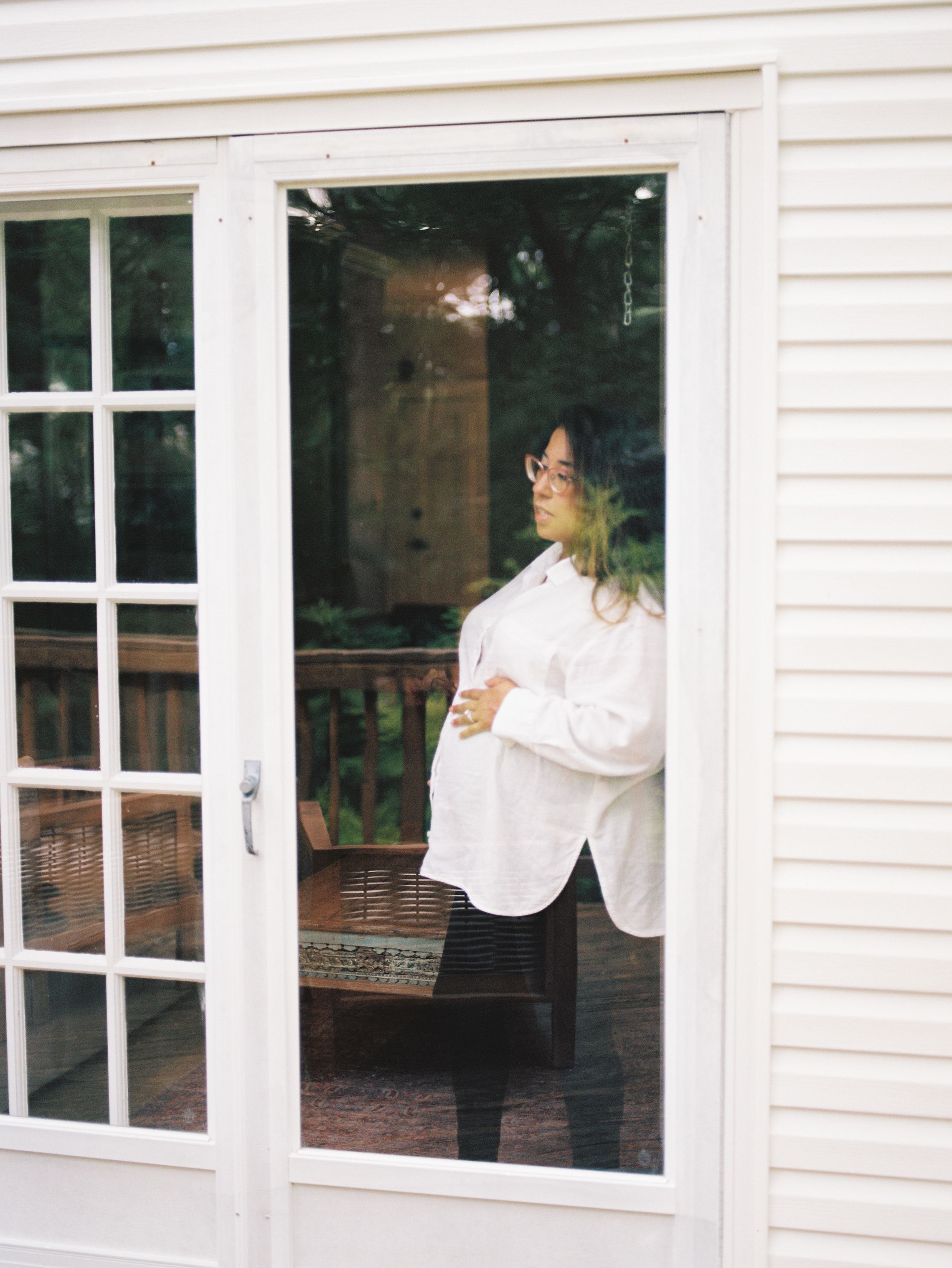 A figure in white shirt stands by white-trimmed windows of a house exterior during daytime.