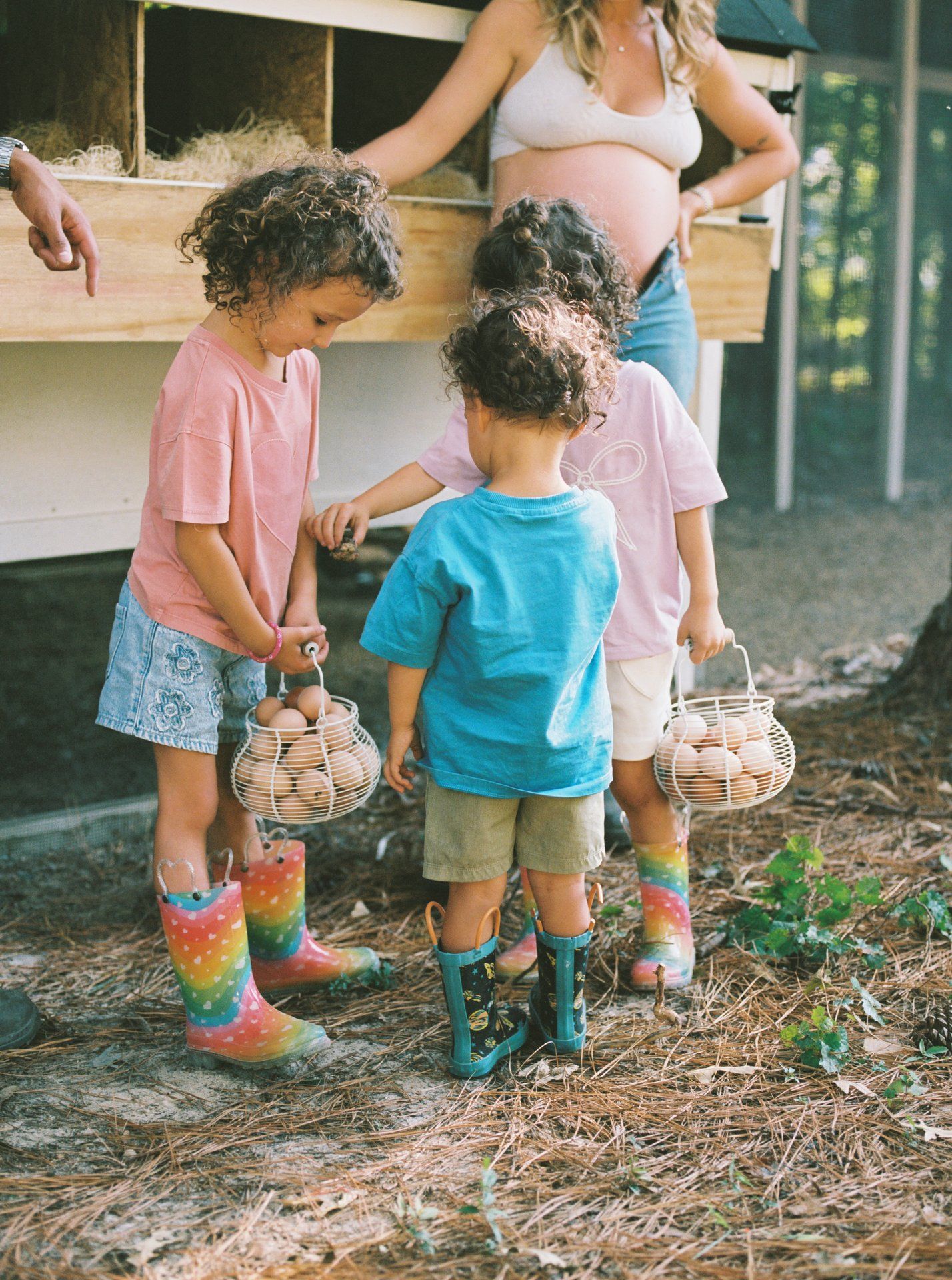 Children wearing colorful rain boots explore the outdoors while gathering items in woven baskets.