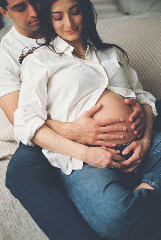 Couple sharing tender maternity moment, man embracing pregnant woman from behind, both cradling baby bump.