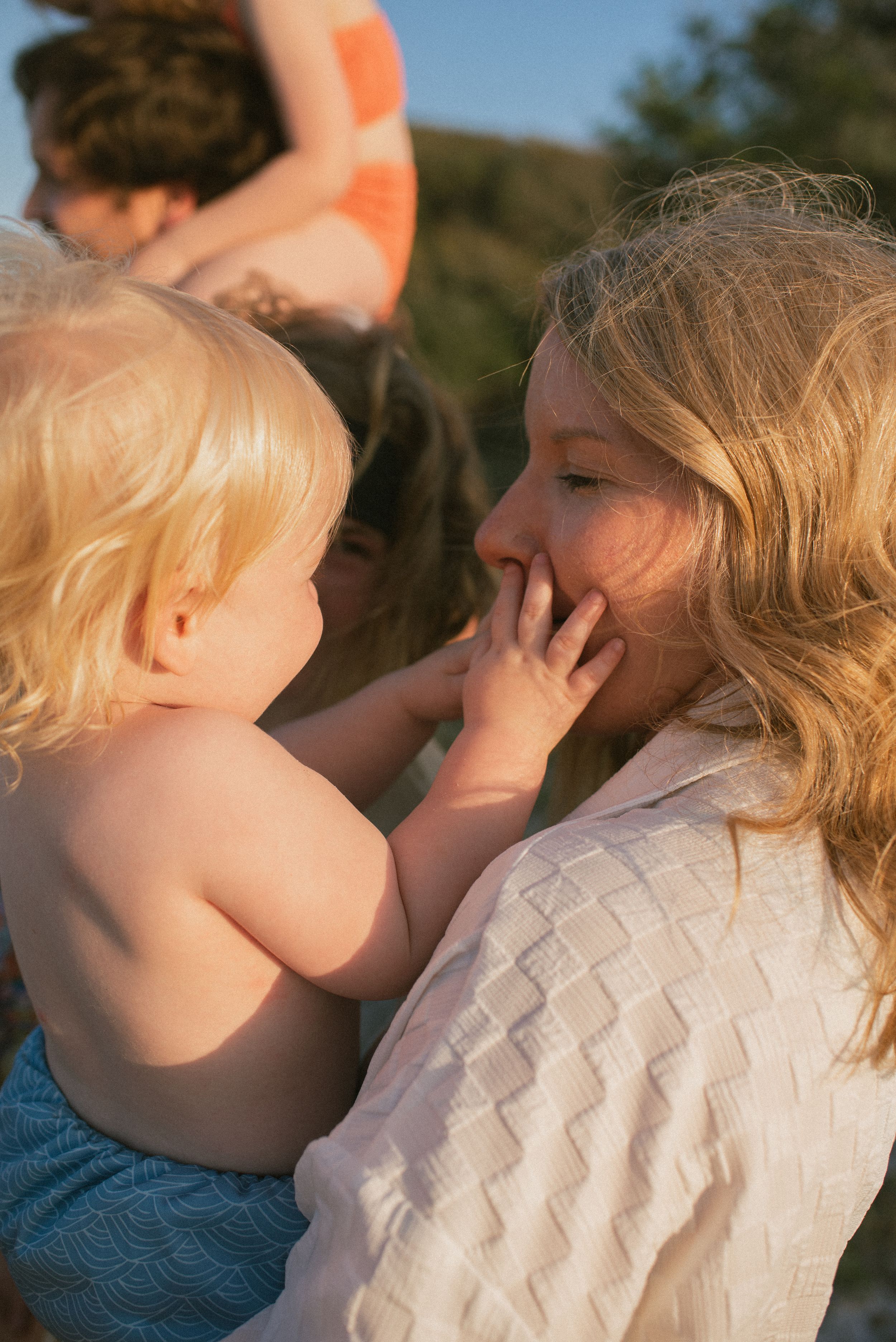 A tender moment is shared between a small baby in denim and a companion in a white sweater in warm sunlight.