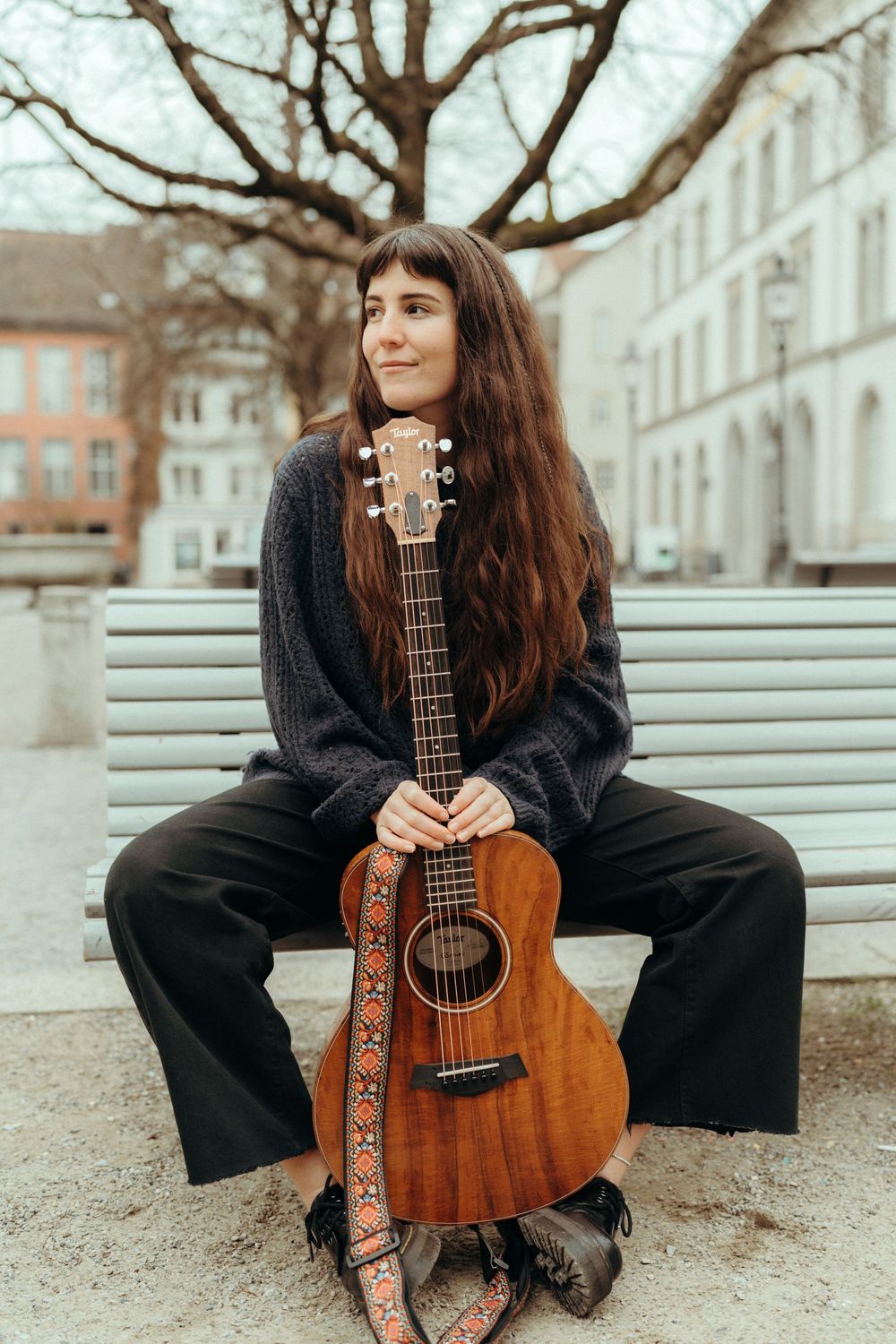Personal branding an lifestyle photography: Young female musician sitting on a bench in Winterthur holding her guitar in between her feet.