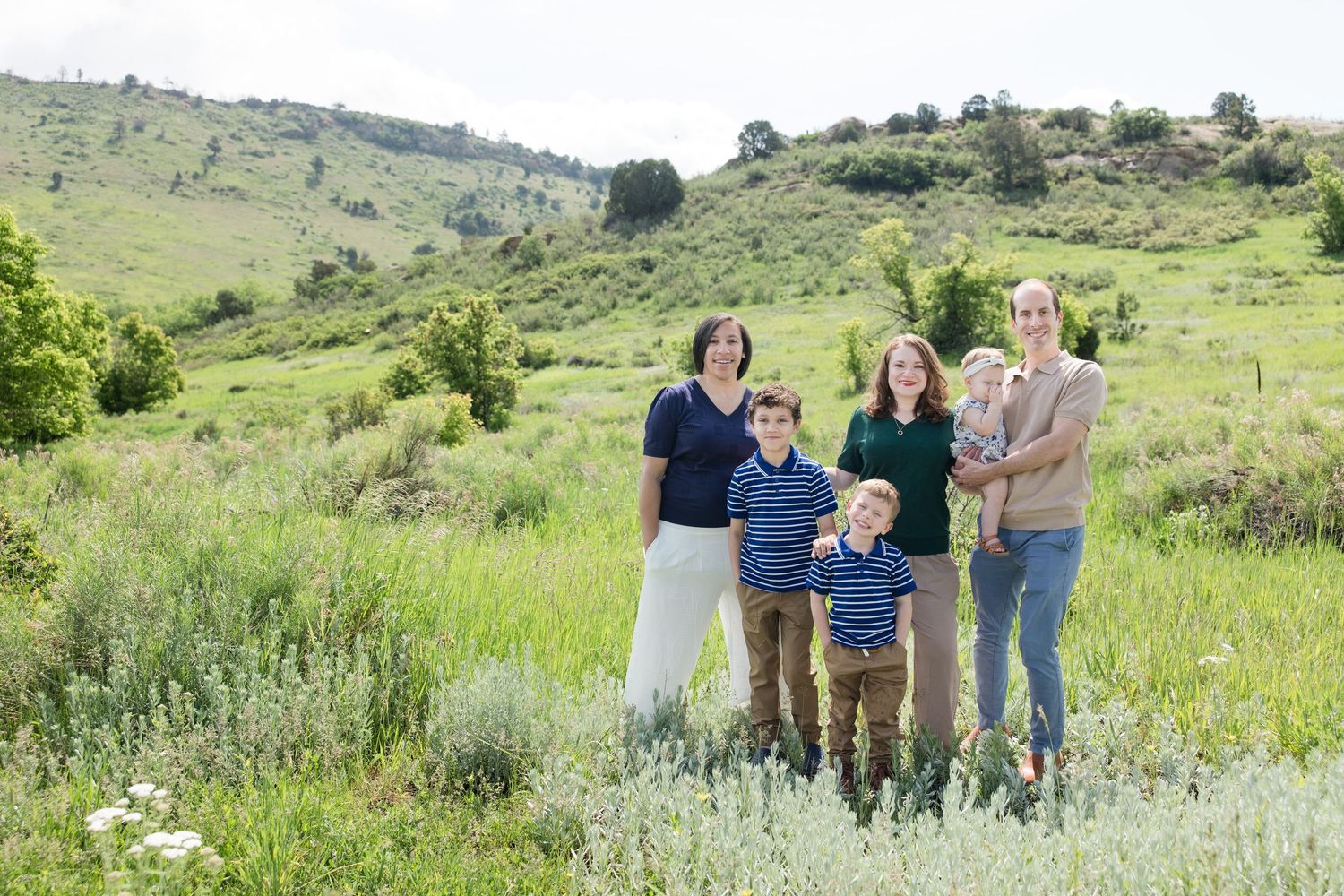 Group photo on a dirt hiking trail with green trees and mountains in the backdrop on a sunny day.