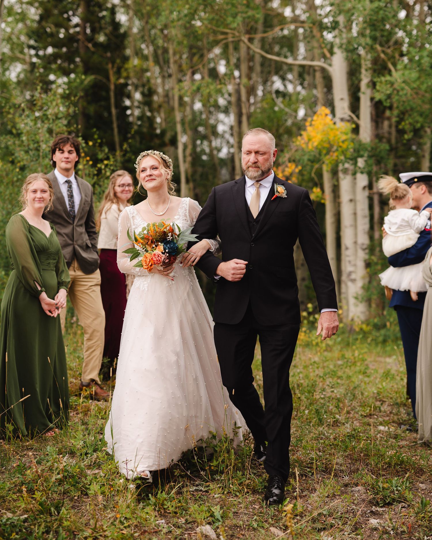 A wedding procession walks through a scenic aspen grove on an autumn day with colorful fall bouquets.