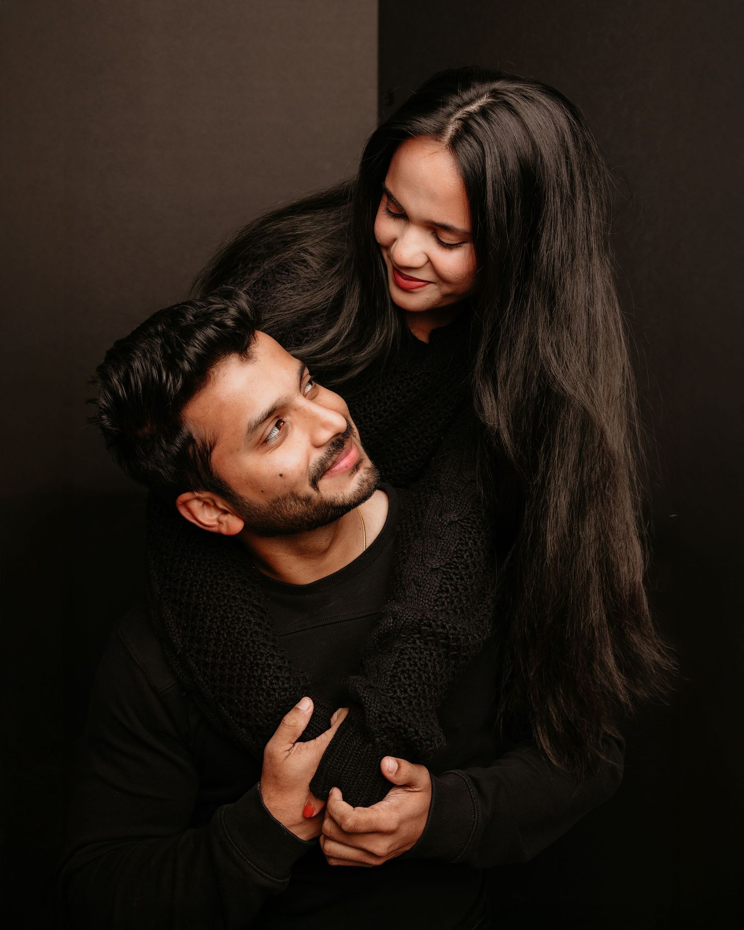 Intimate couple portrait in black sweaters against dark background.