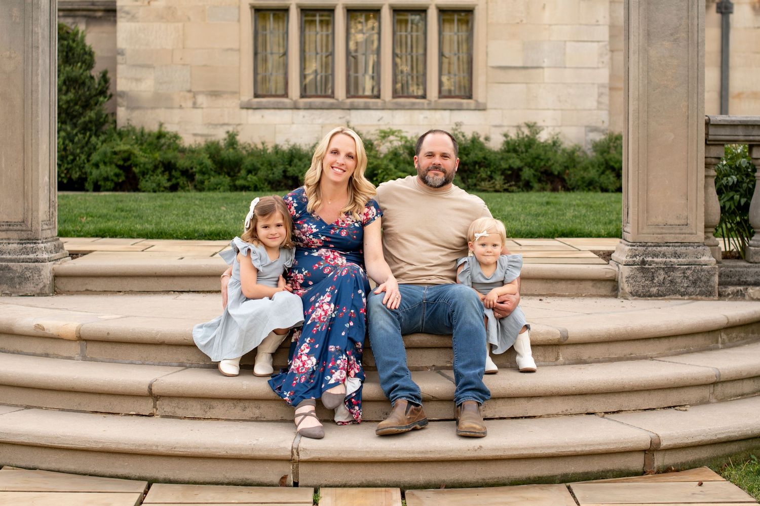 A family of four sitting on stone steps in front of a Gothic style building with decorative architecture.