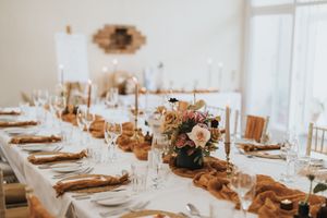 Wedding reception tables styled in neutral beige and white with glass chargers and floral centerpieces.