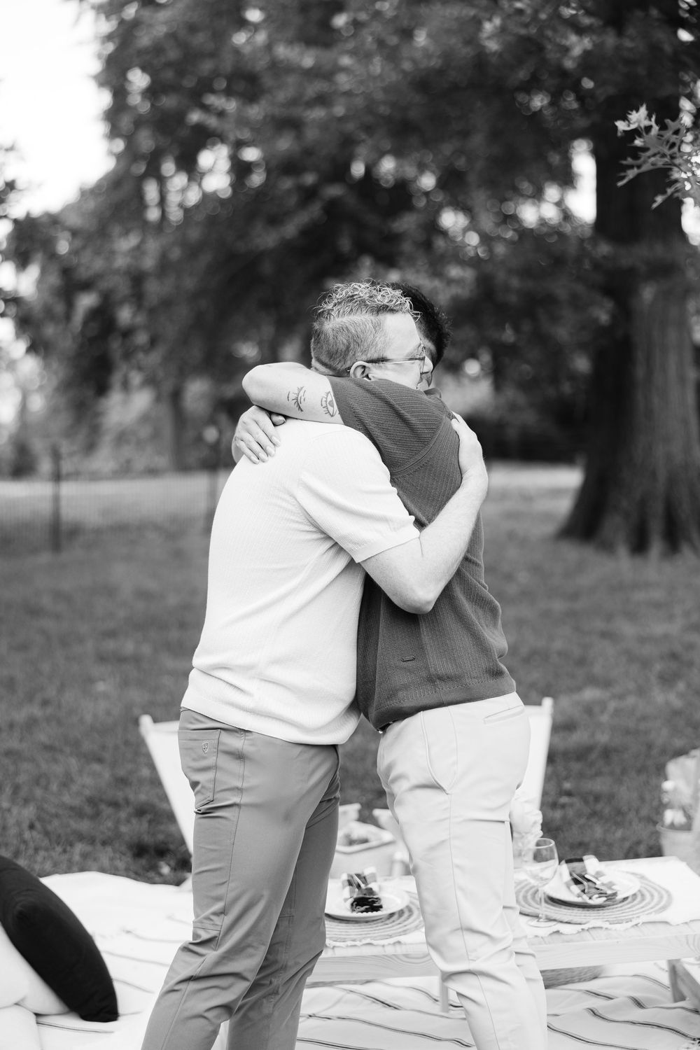 A tender embrace between two people standing on a blanket in a park setting captured in black and white.