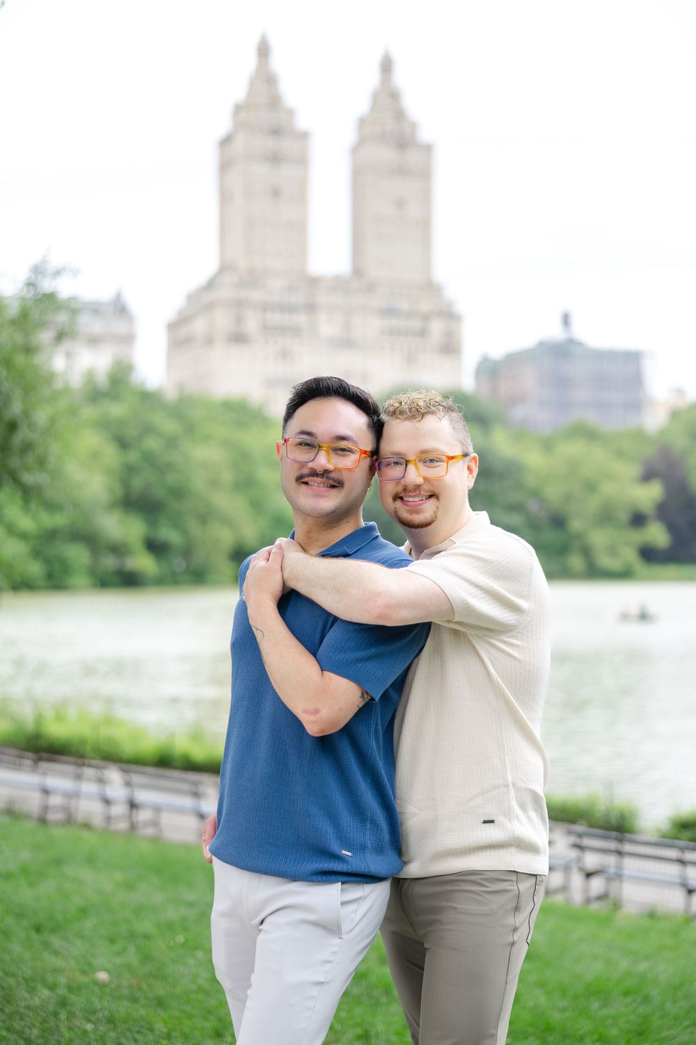 An engaged couple shares an intimate moment on a Cherry Hill overlooking the Central Park Lake with NYC buildings in view.
