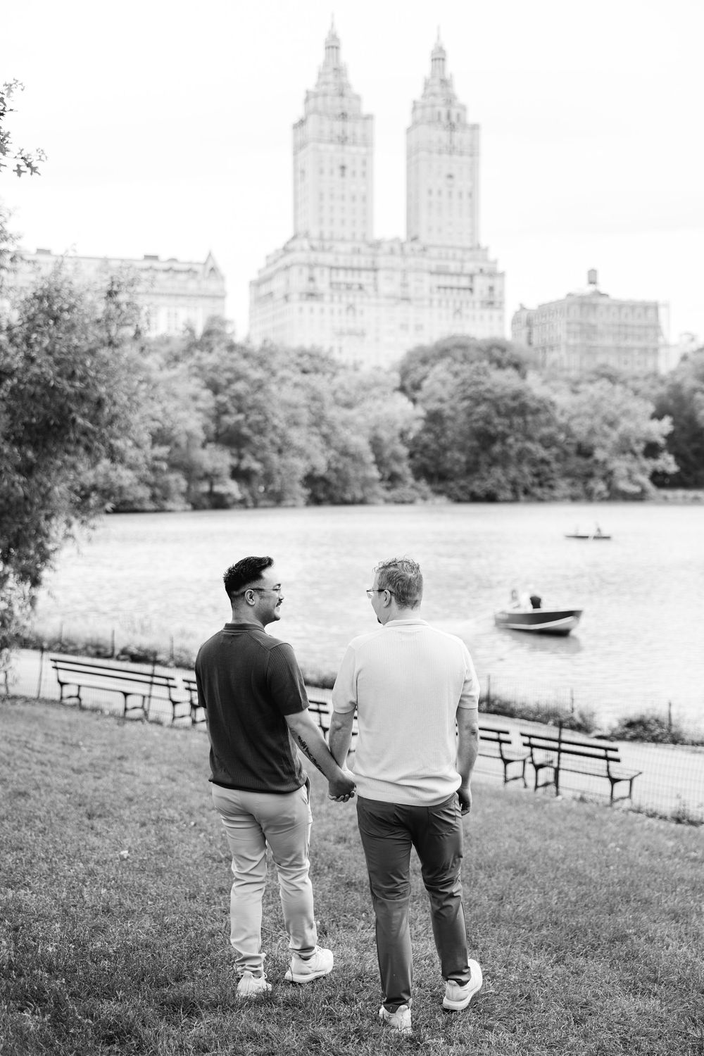 A black and white photo of a couple strolling along Central Park Lake with the Upper West Side skyline visible.