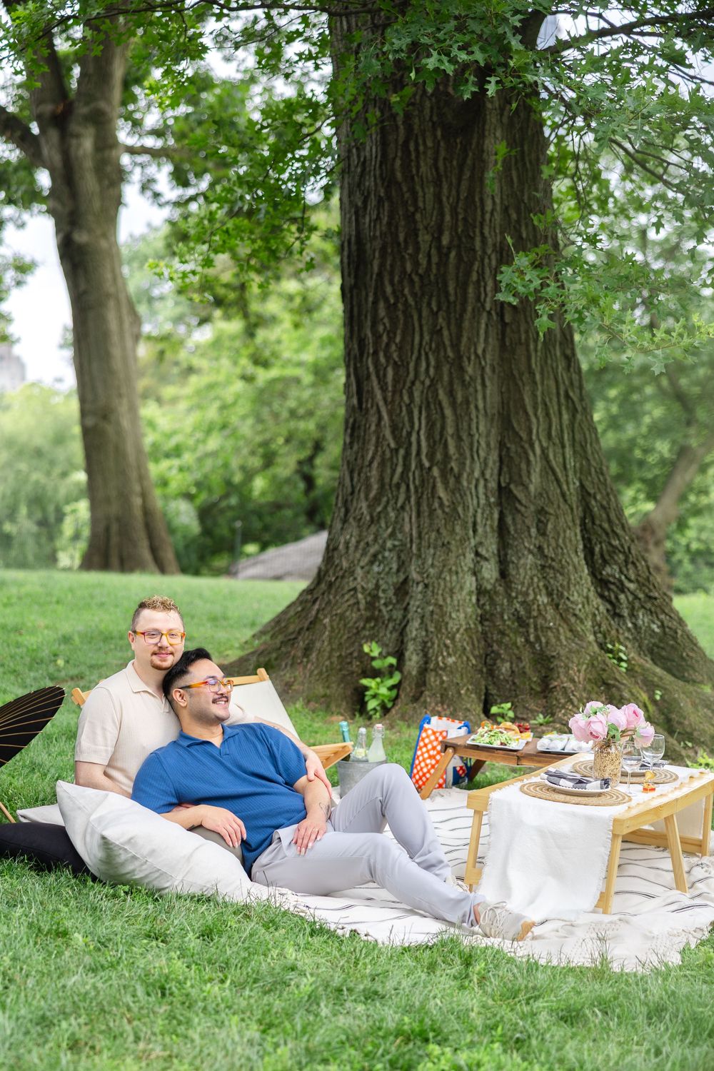 A couple shares a relaxing moment on a blanket during a sunny afternoon picnic proposal in Central Park.