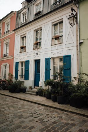 Jolie façade blanche aux volets bleus sur rue pavée, charme architectural européen.