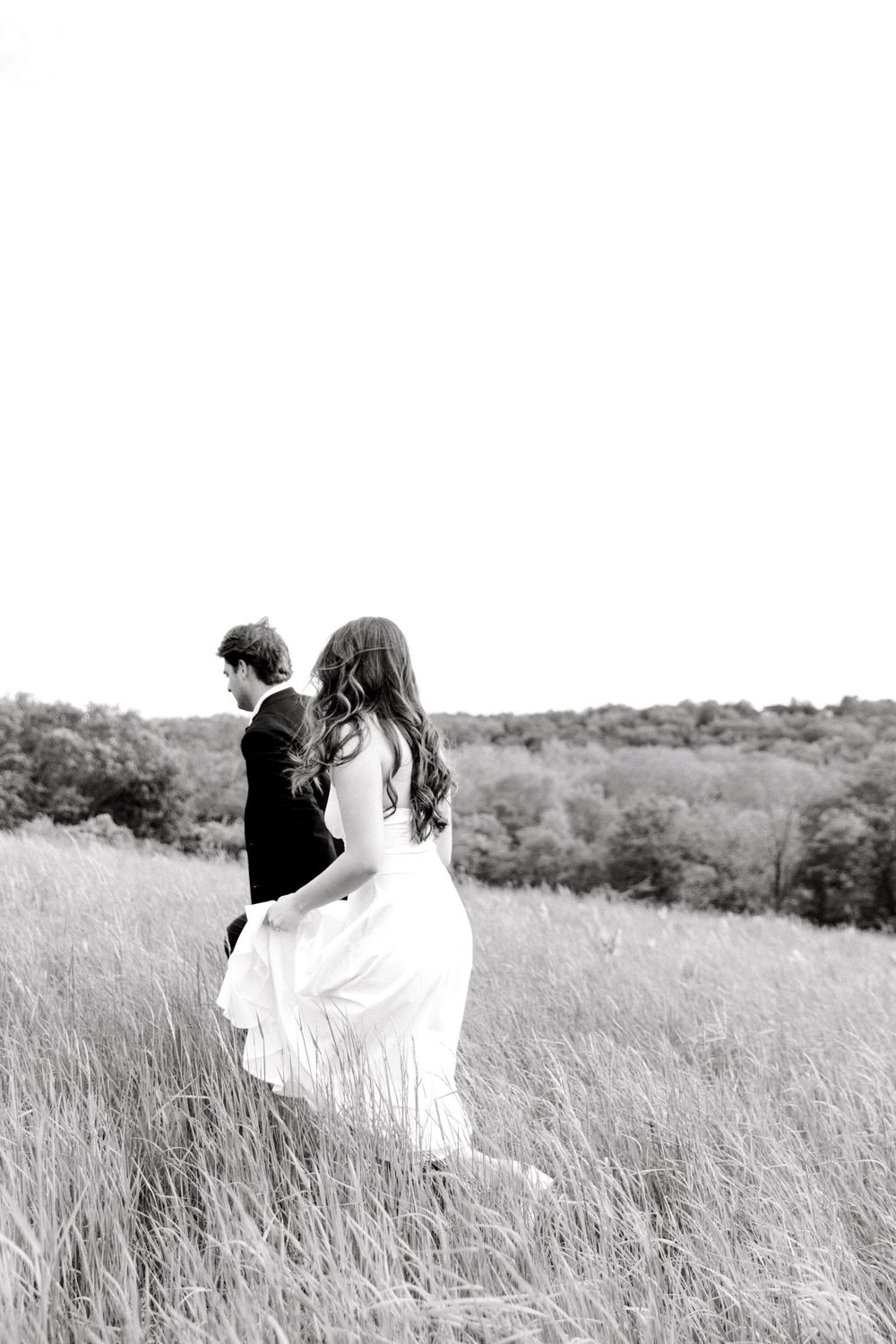 Engaged couple walking hand-in-hand through the tall grass at Natirar Park in Peapack, NJ.