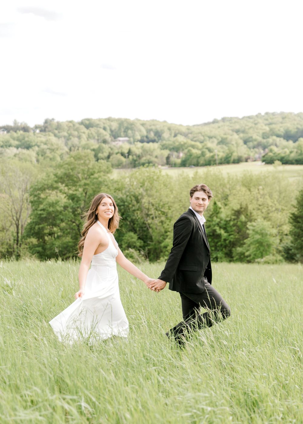 Engaged couple walking hand-in-hand through the tall grass at Natirar Park in Peapack, NJ.