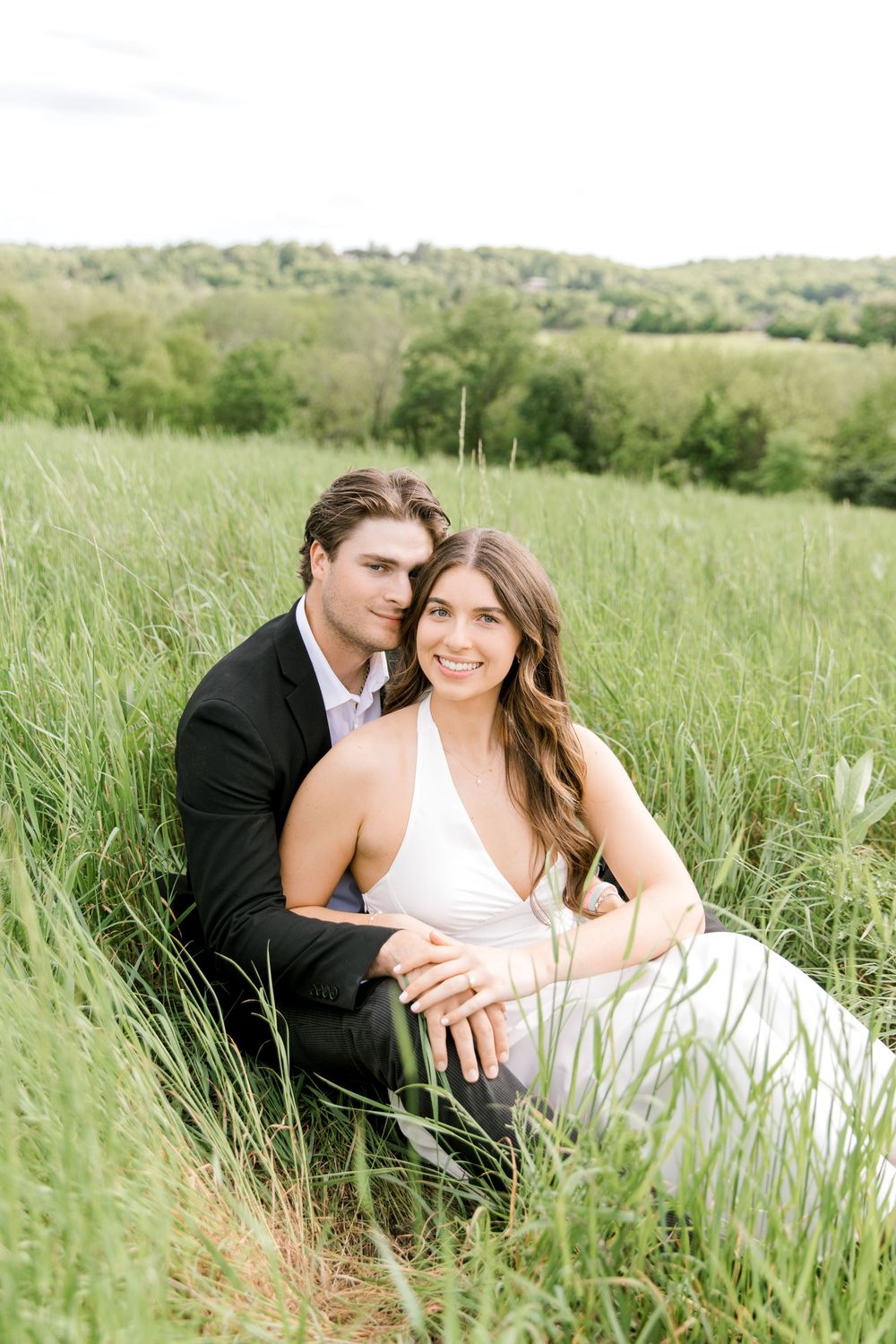 Engaged couple sitting in the tall grass at Natirar Park in Peapack, NJ.