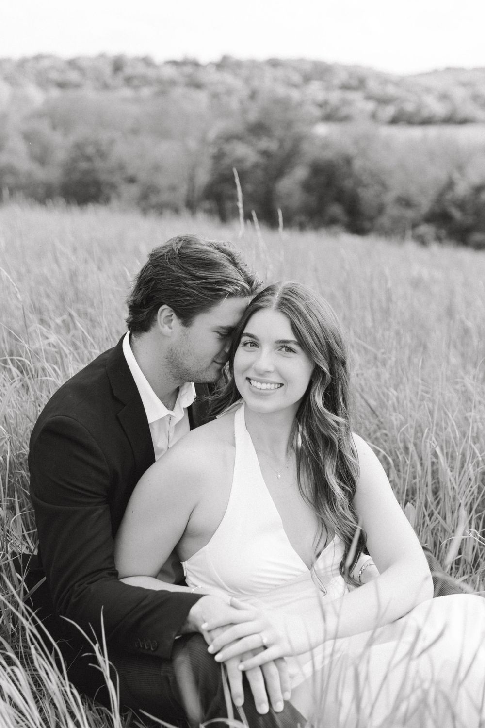 Engaged couple sitting in the tall grass at Natirar Park in Peapack, NJ.
