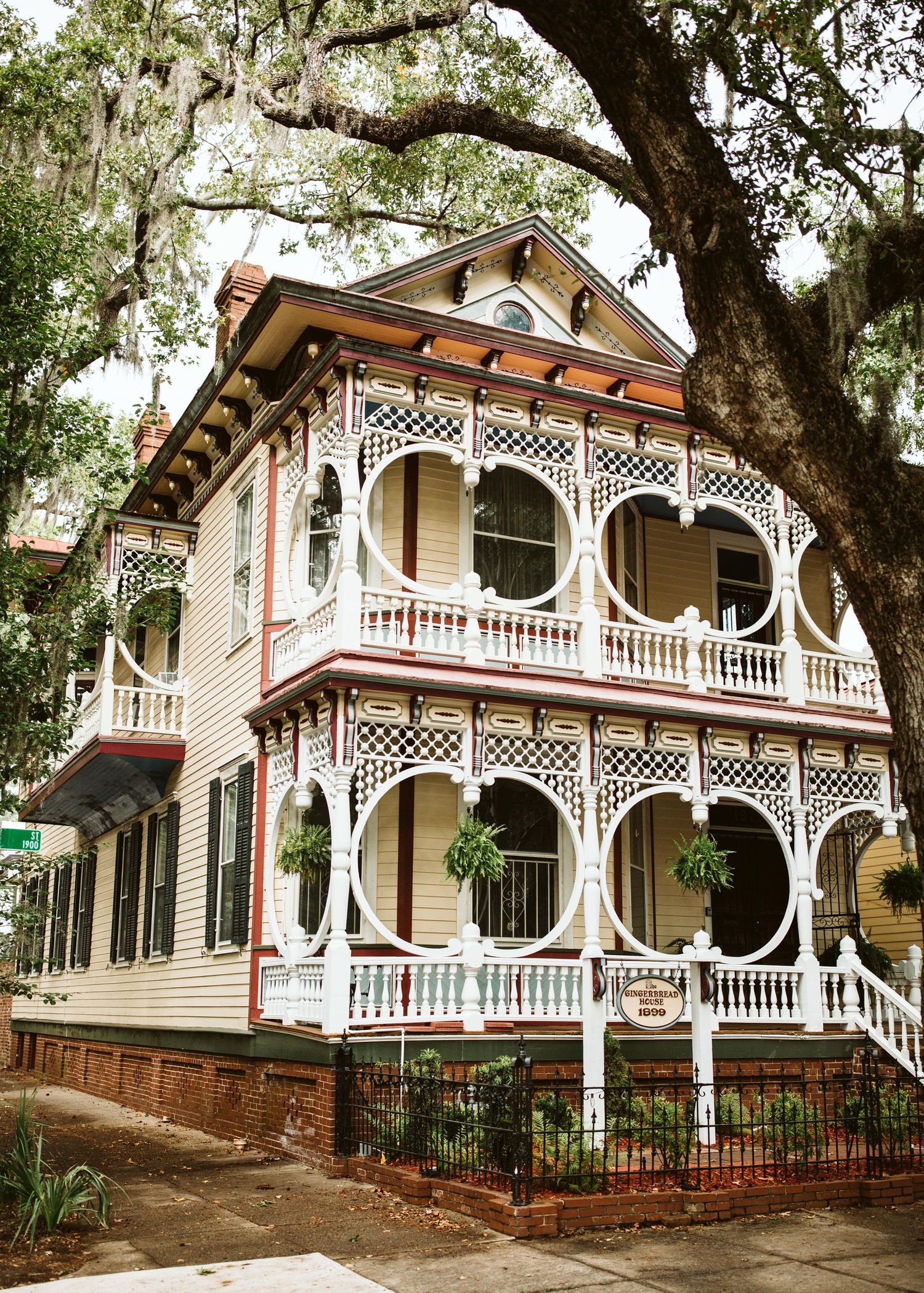 Victorian-style house with ornate white gingerbread trim and wraparound porch under Spanish moss.