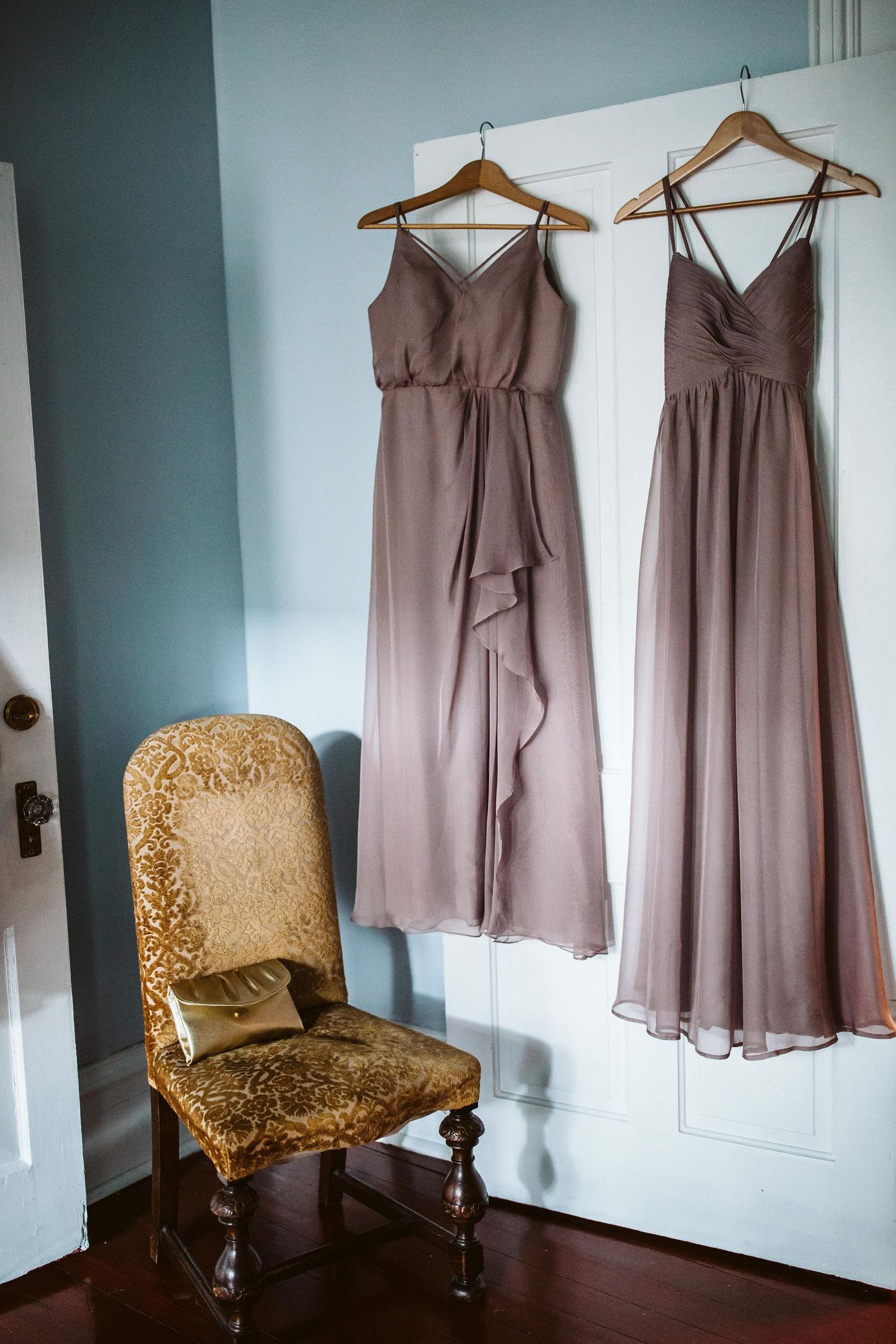 Mauve bridesmaid dresses hanging on wall next to vintage upholstered chair.