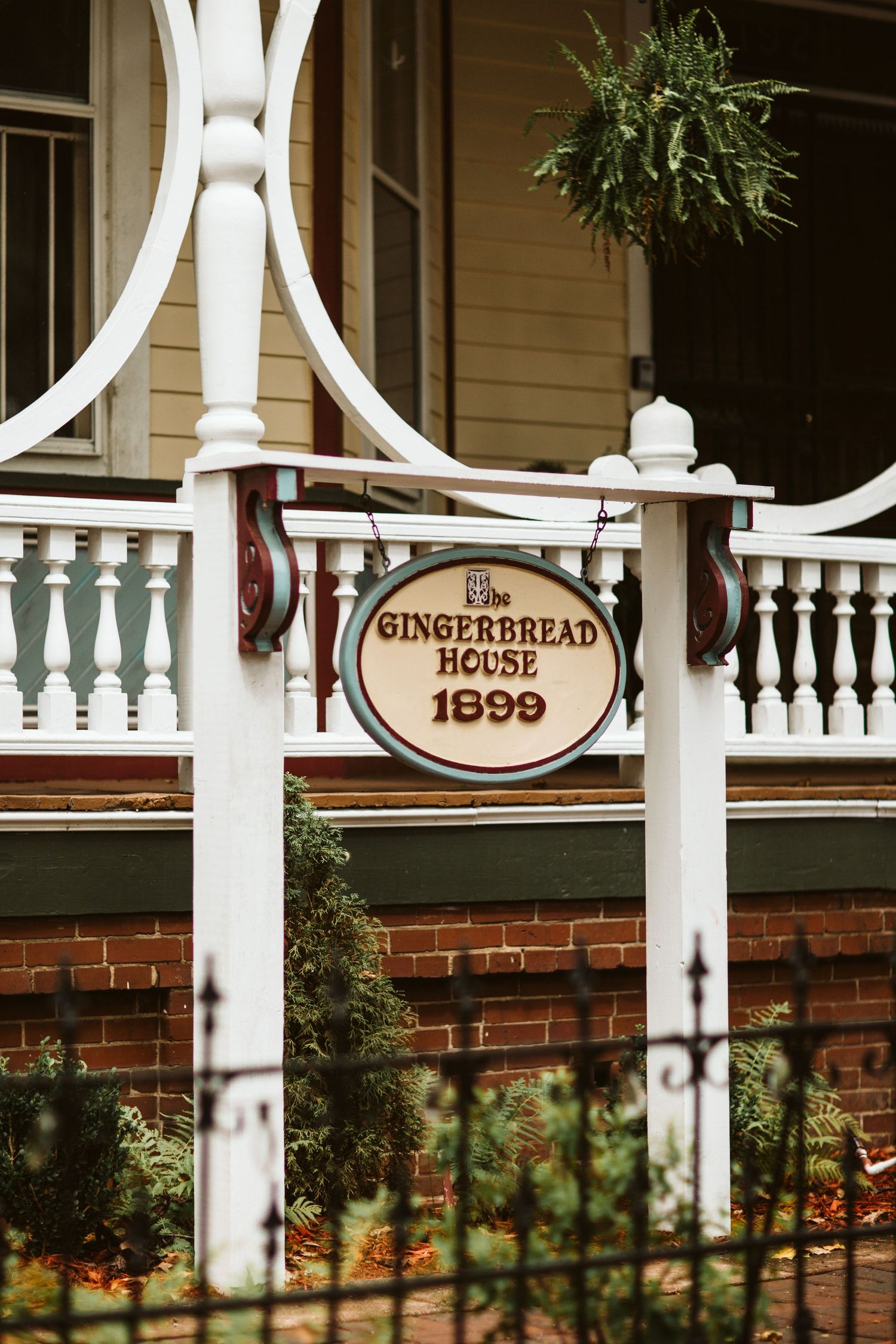 Vintage white gingerbread house sign from 1899 on ornate porch railing.