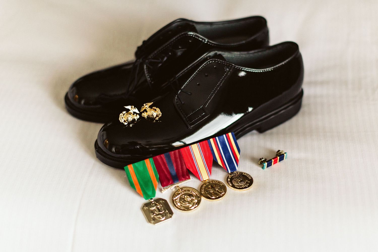 Military dress shoes and medals displayed on white surface.