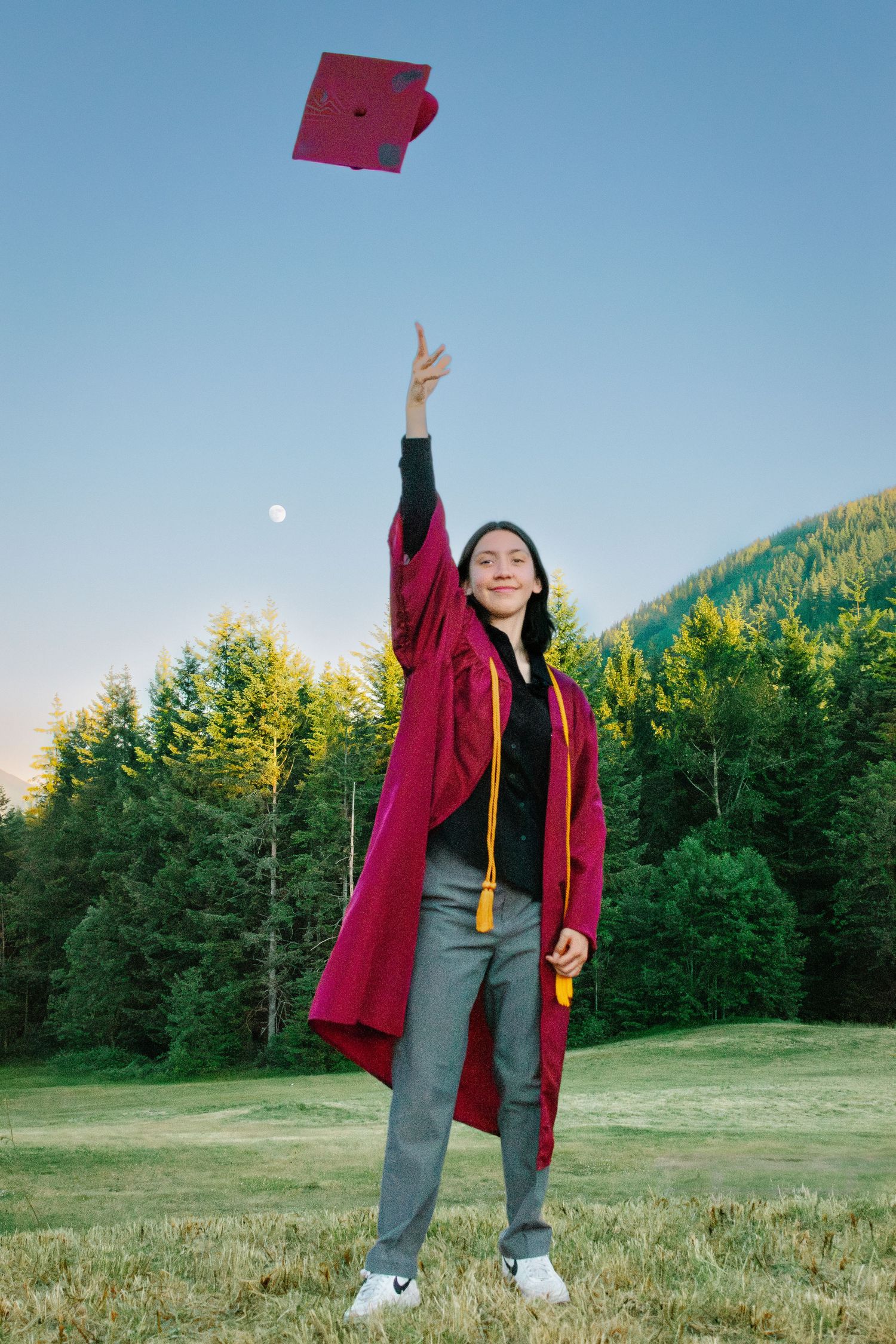 Graduate tossing cap in the air under a rising moon at Snoqualmie Point Park. Seattle graduation photography.