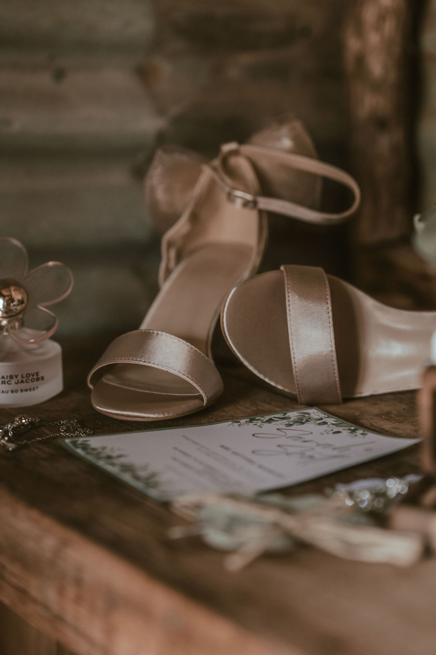 Brown leather sandals and wedding stationary arranged in a warm, vintage style composition on a wooden surface.