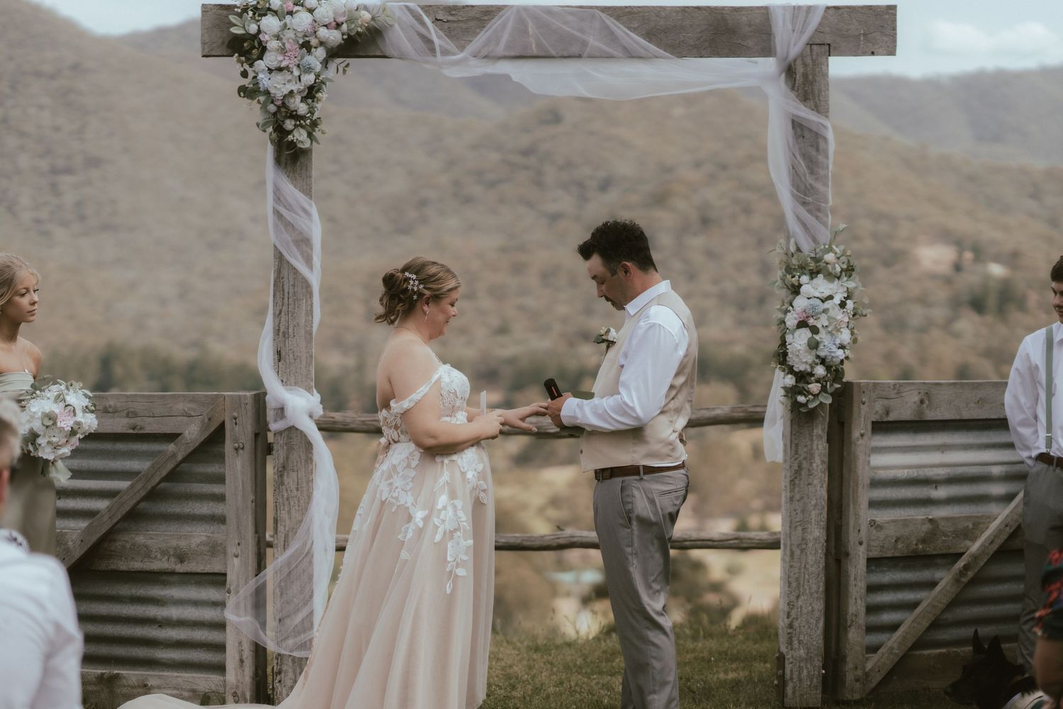 Outdoor rustic wedding scene with wooden fences and mountains in the background.