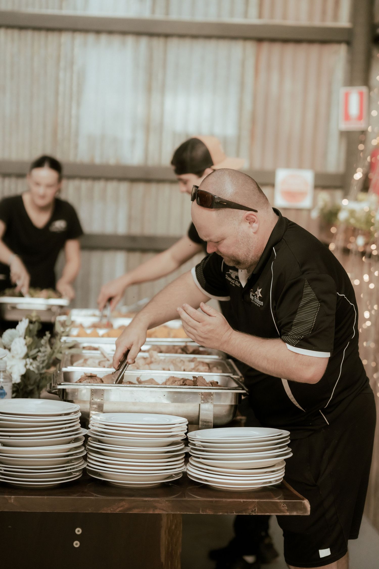 Professional caterer arranges plates and prepares food on a rustic wooden table during an event.