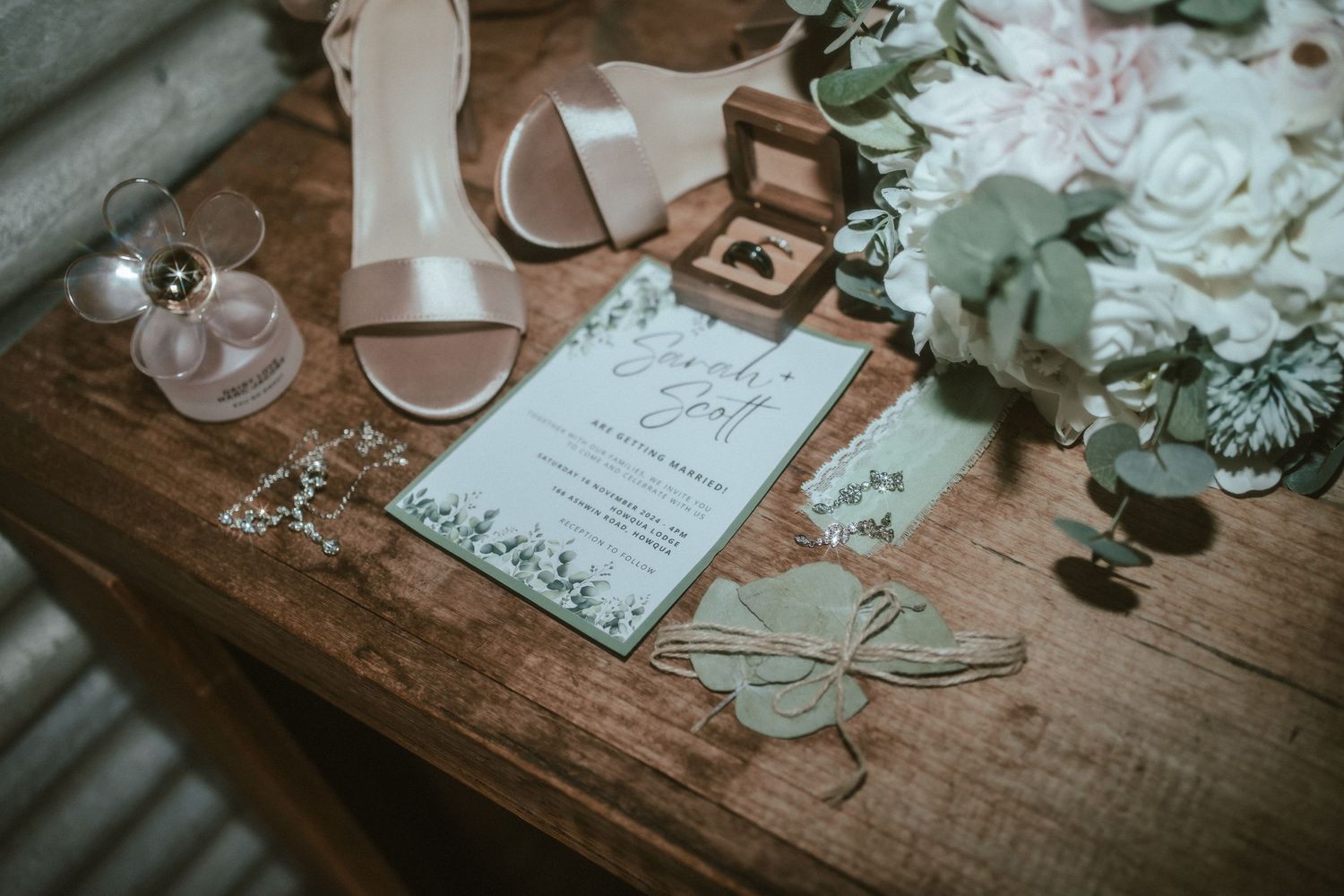 Wedding accessories and decor including white flowers, rings, and invitations arranged on a rustic wooden surface.