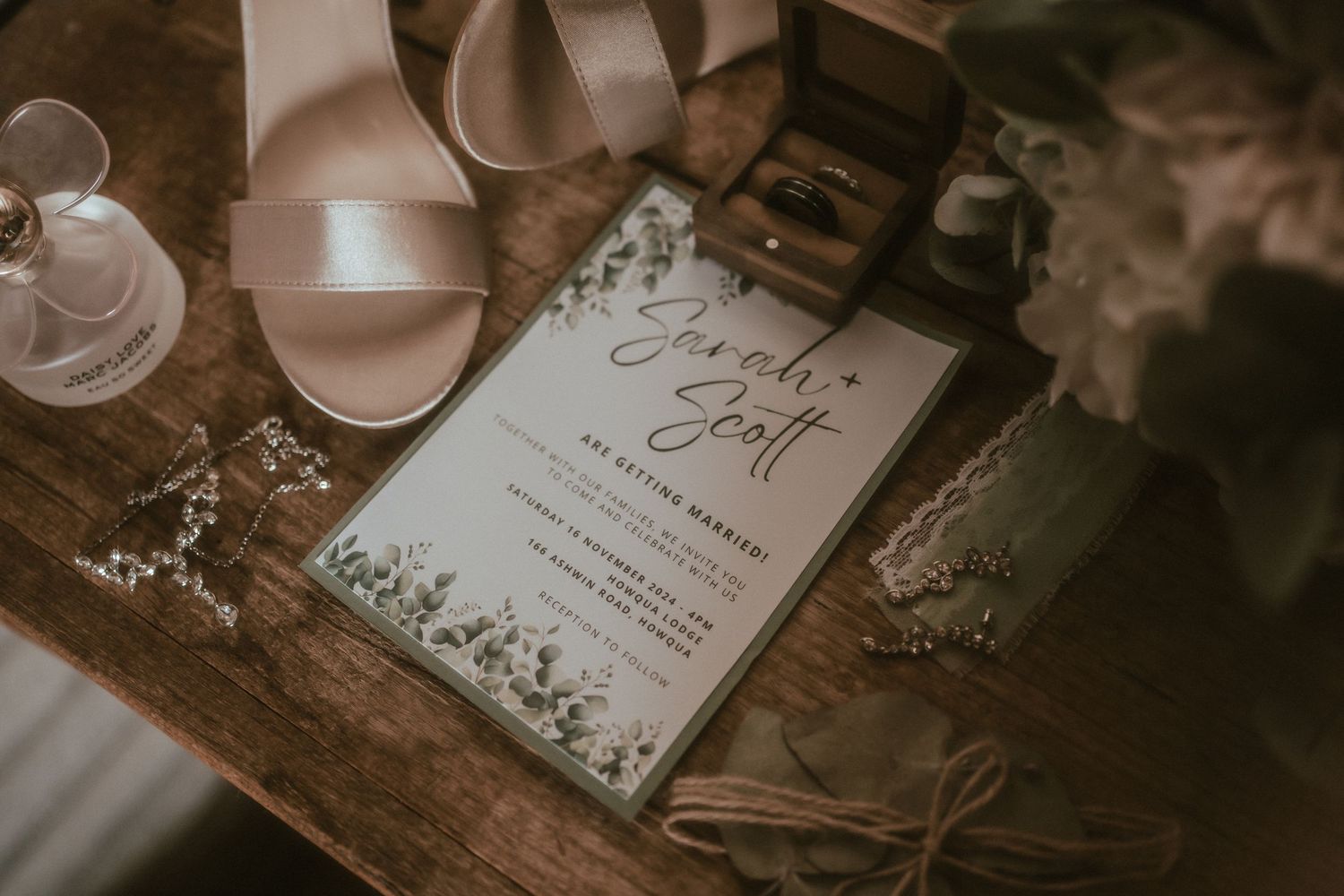 Wedding invitation and bridal accessories arranged on rustic wooden table with soft sepia tones.