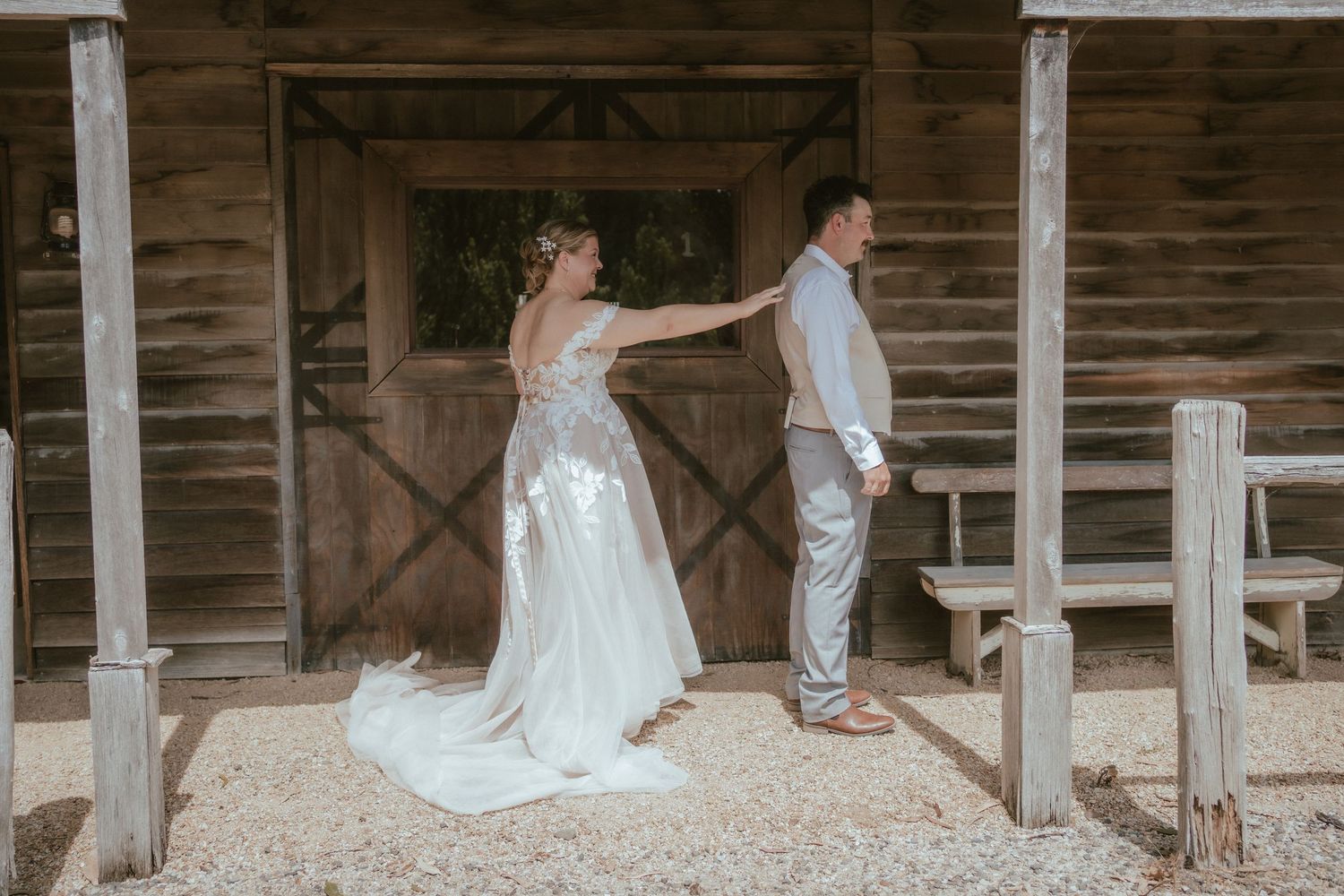 A couple in wedding attire standing back to back on a rustic wooden porch.