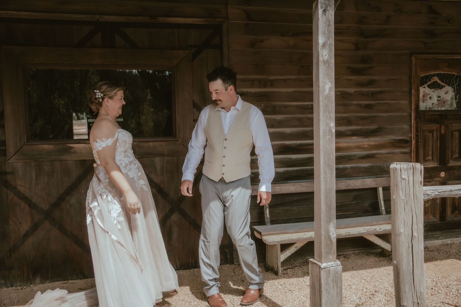 A couple in wedding attire share a moment together on a rustic wooden porch of a barn.