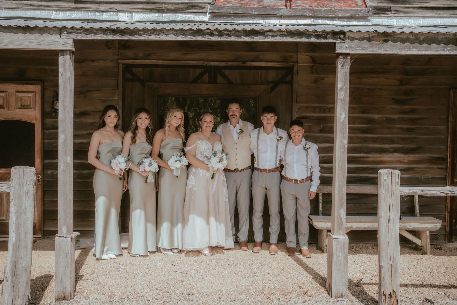 Rustic wedding party poses on wooden porch of barn with vintage farmhouse charm.