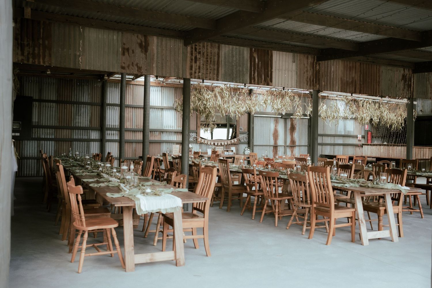 A rustic reception venue with wooden chairs and tables arranged under vintage chandeliers in an industrial-style space.