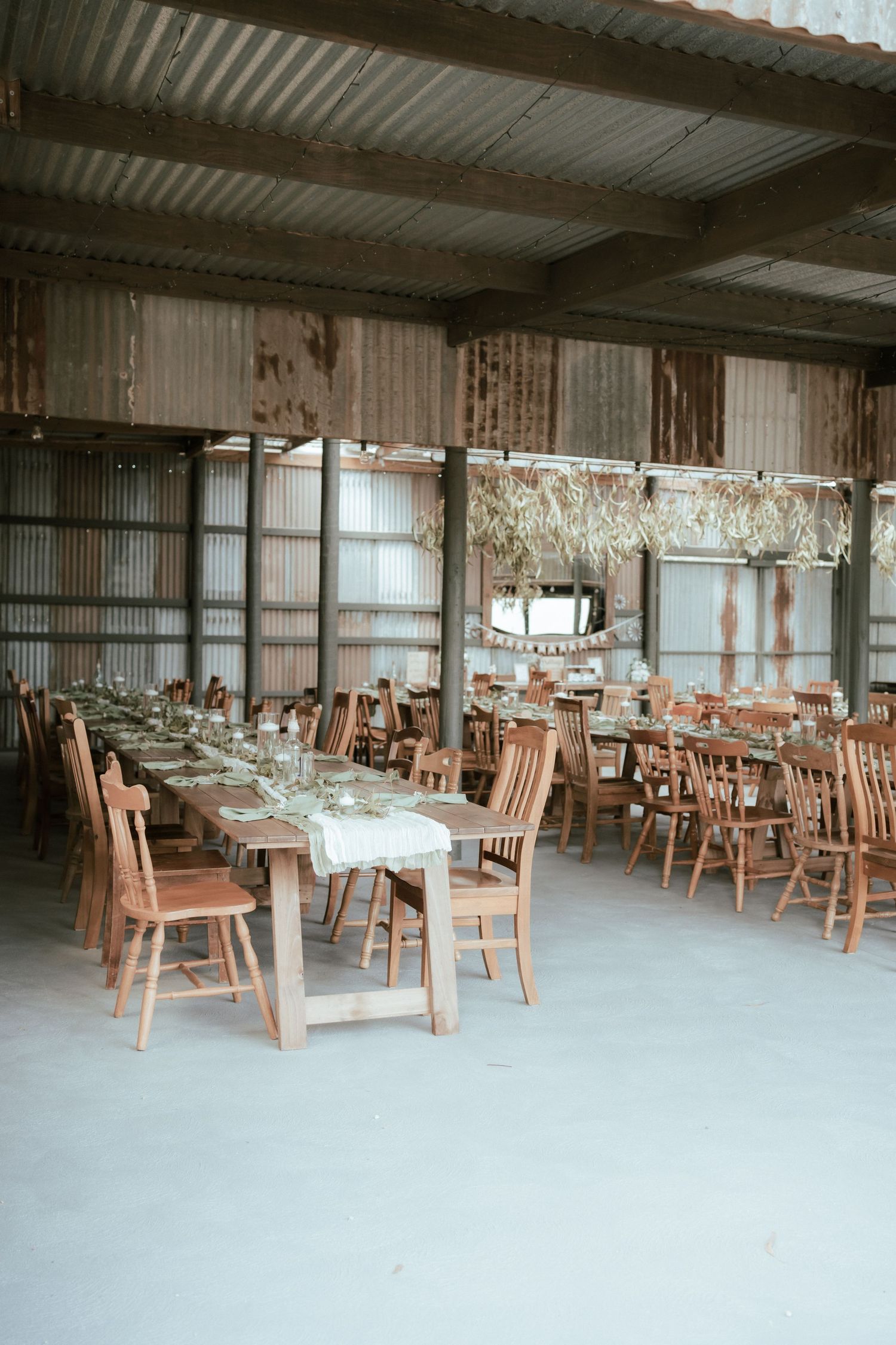 Rustic wedding reception venue with wooden tables and chairs set up in an industrial-style space with corrugated metal walls.