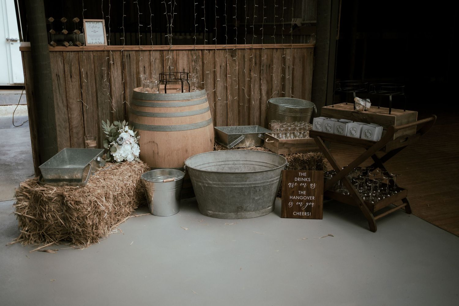 Rustic wedding decor featuring hay bales, wine barrels, and vintage metal tubs arranged on a light floor.