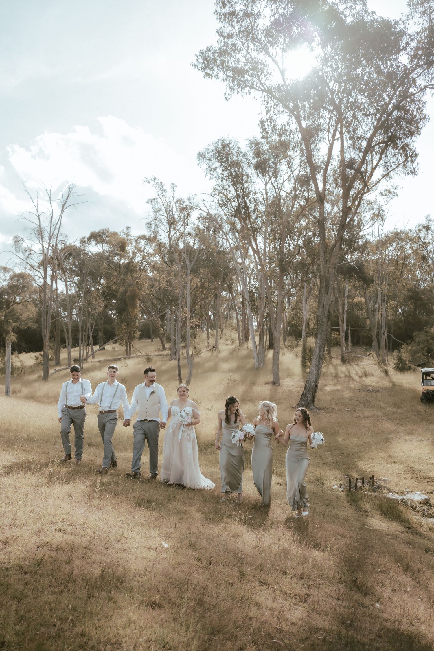 A wedding party walks through a scenic woodland setting with tall eucalyptus trees on a sunny afternoon.