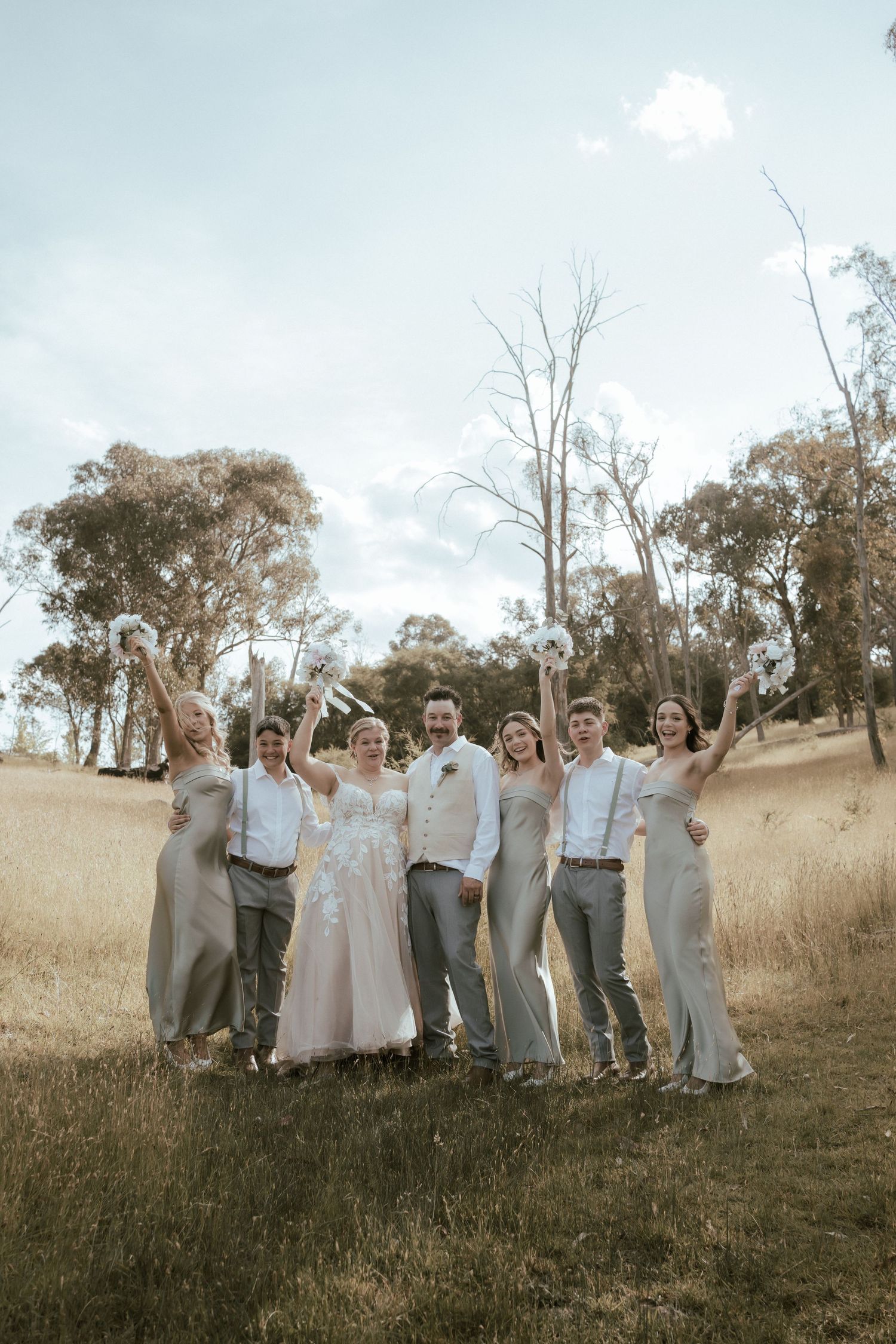 Wedding party poses together in a golden field with eucalyptus trees in the background.