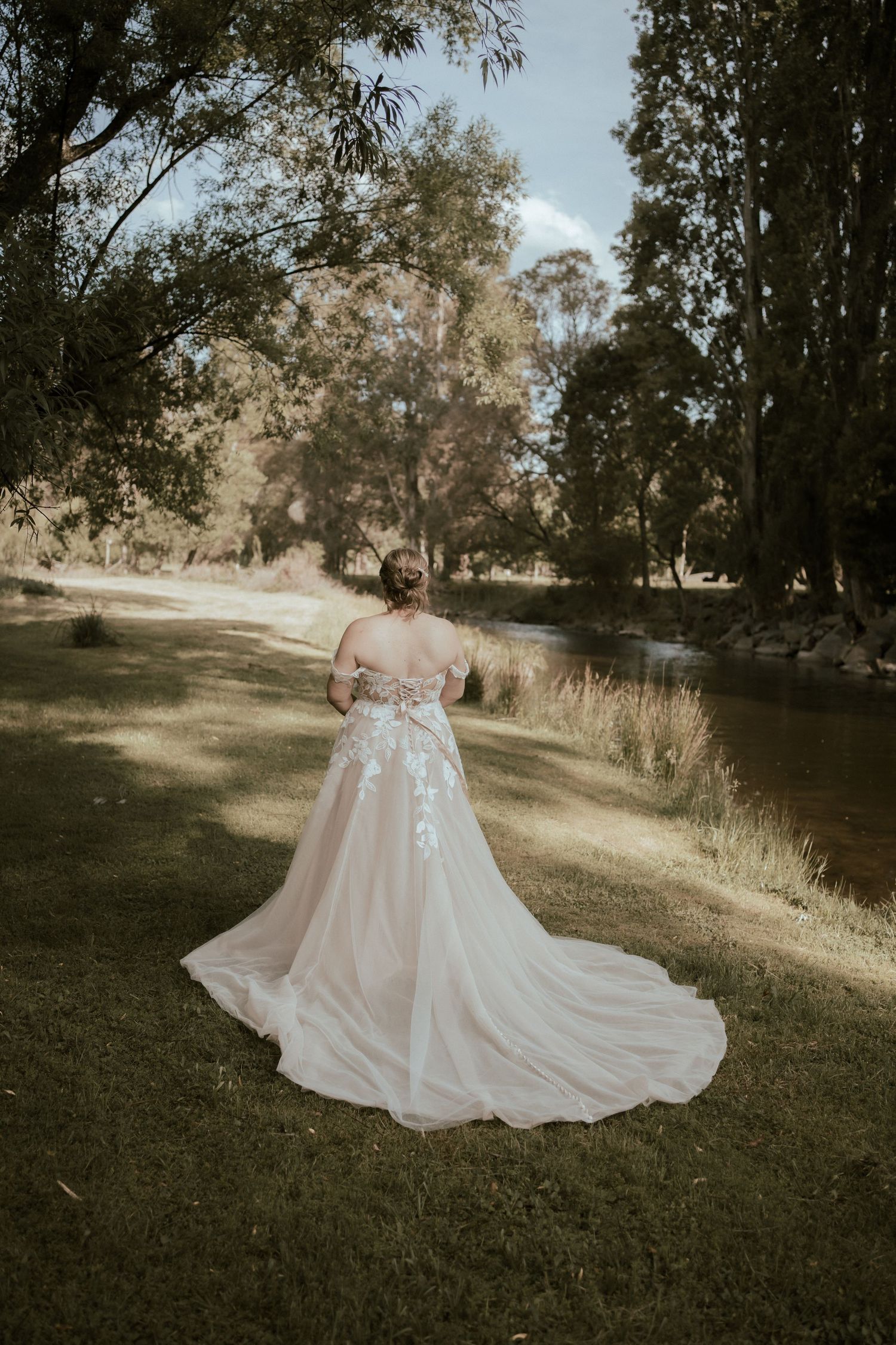 A romantic outdoor wedding photoshoot with a flowing blush pink gown trailing on grassy grounds at sunset.