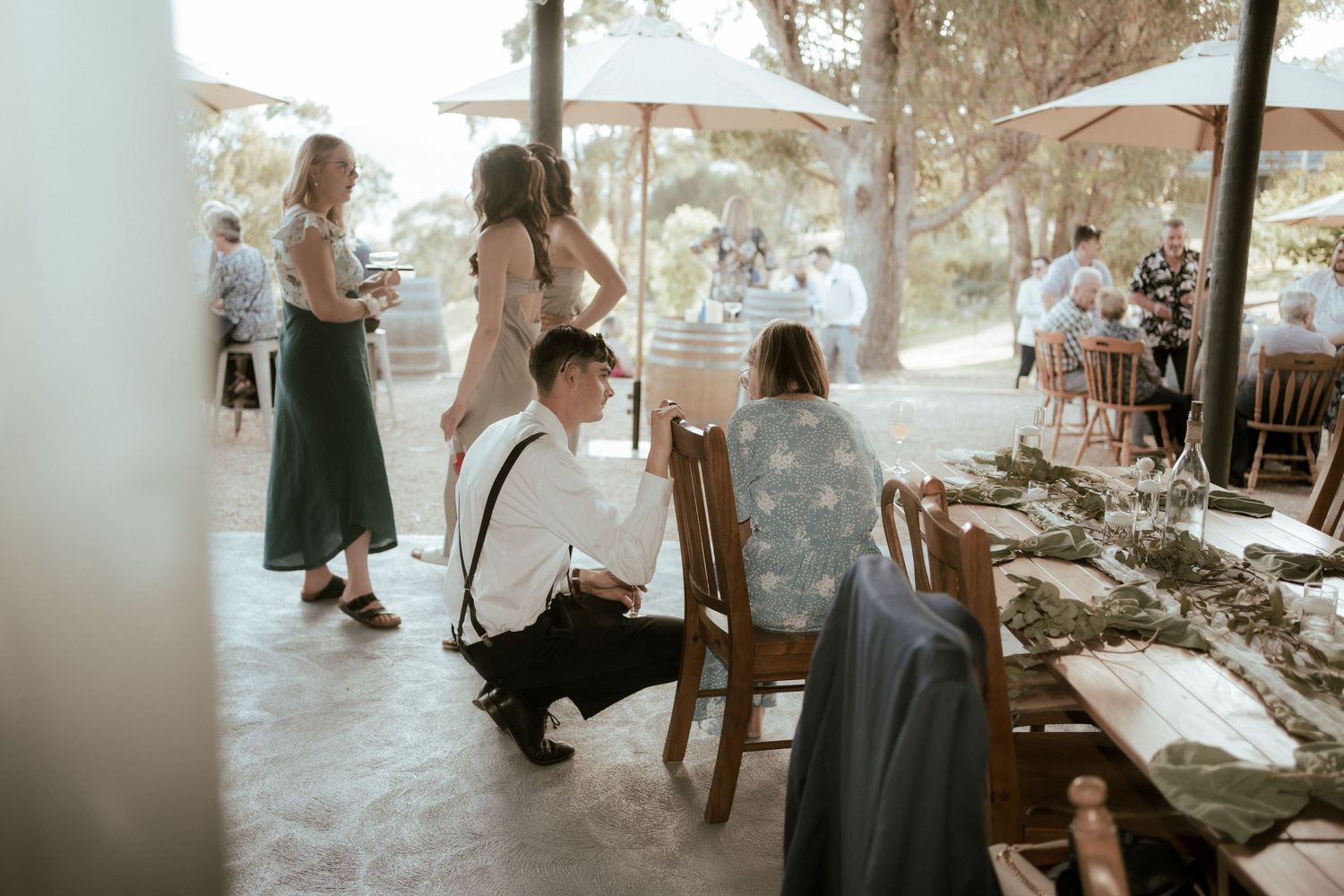 Wedding reception guests mingle and dine at tables set under a covered outdoor venue space.