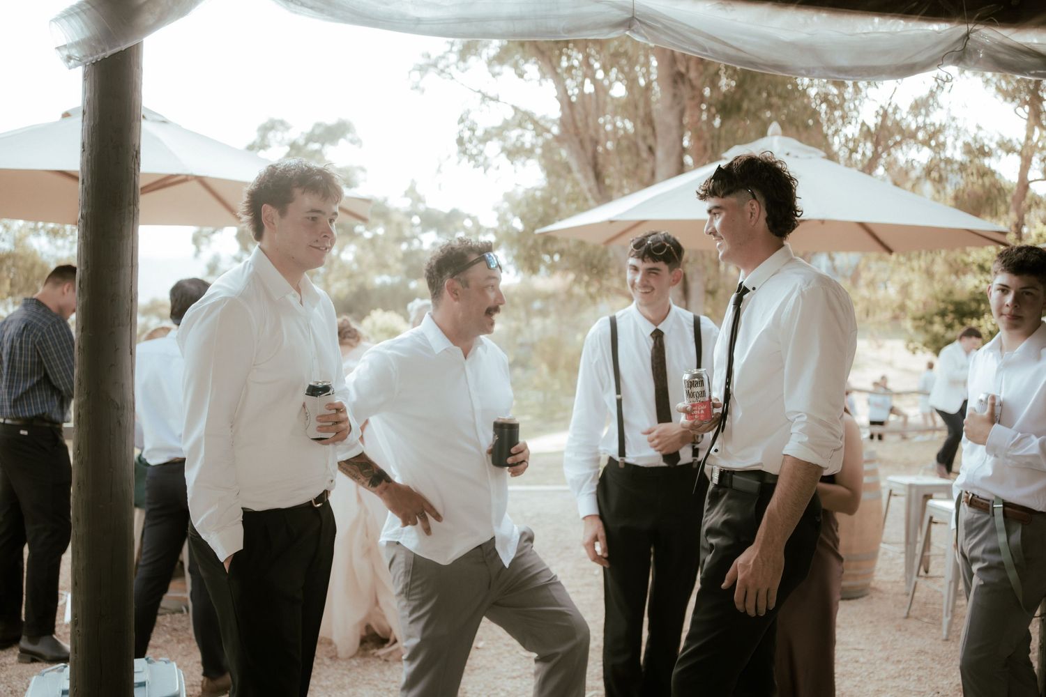 A group of people in formal attire gathered outdoors under a covered area at a social event or celebration.