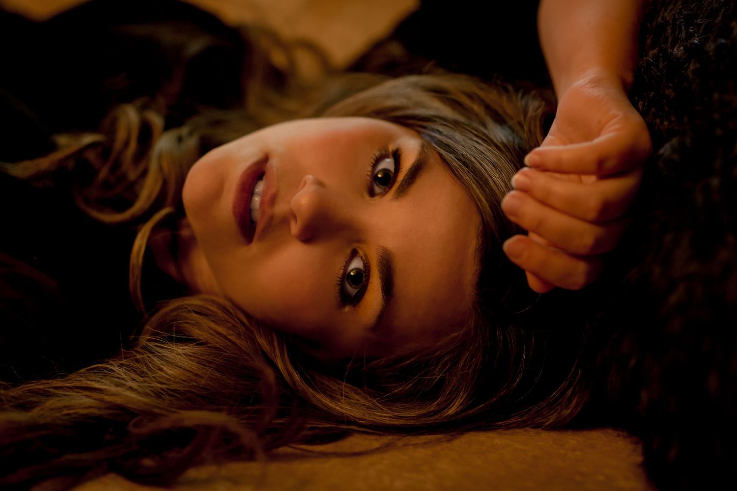 Close-up portrait of a young woman lying down with long hair and expressive brown eyes.