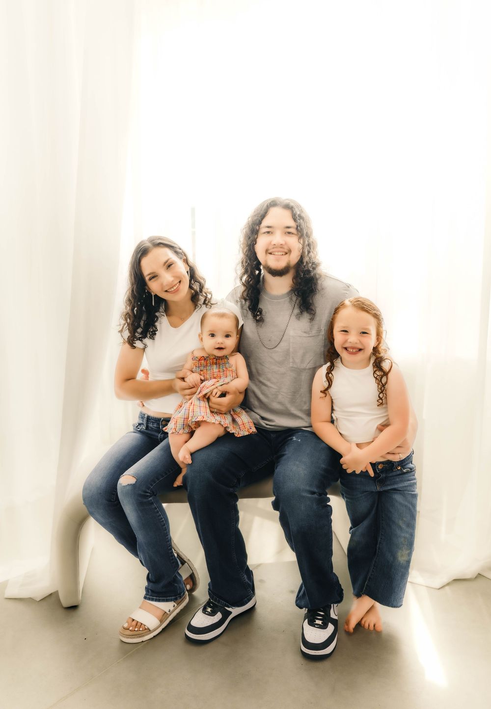 Family sitting together on a bench in coordinated casual outfits during a studio photoshoot.