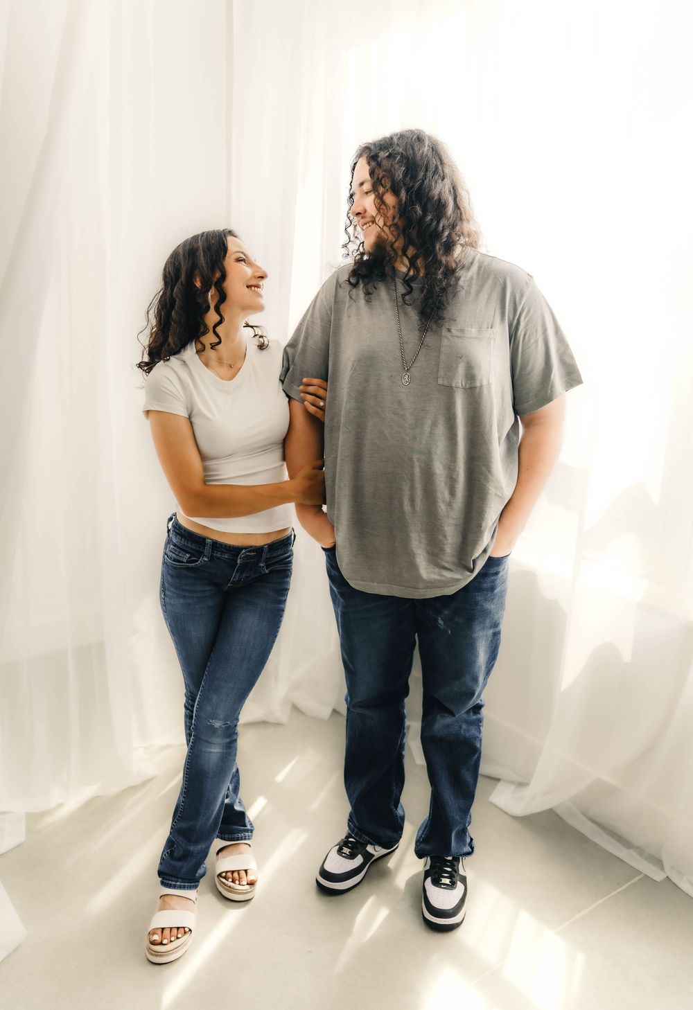 Casual lifestyle portraits of a couple laughing and interacting in a minimalist white studio.