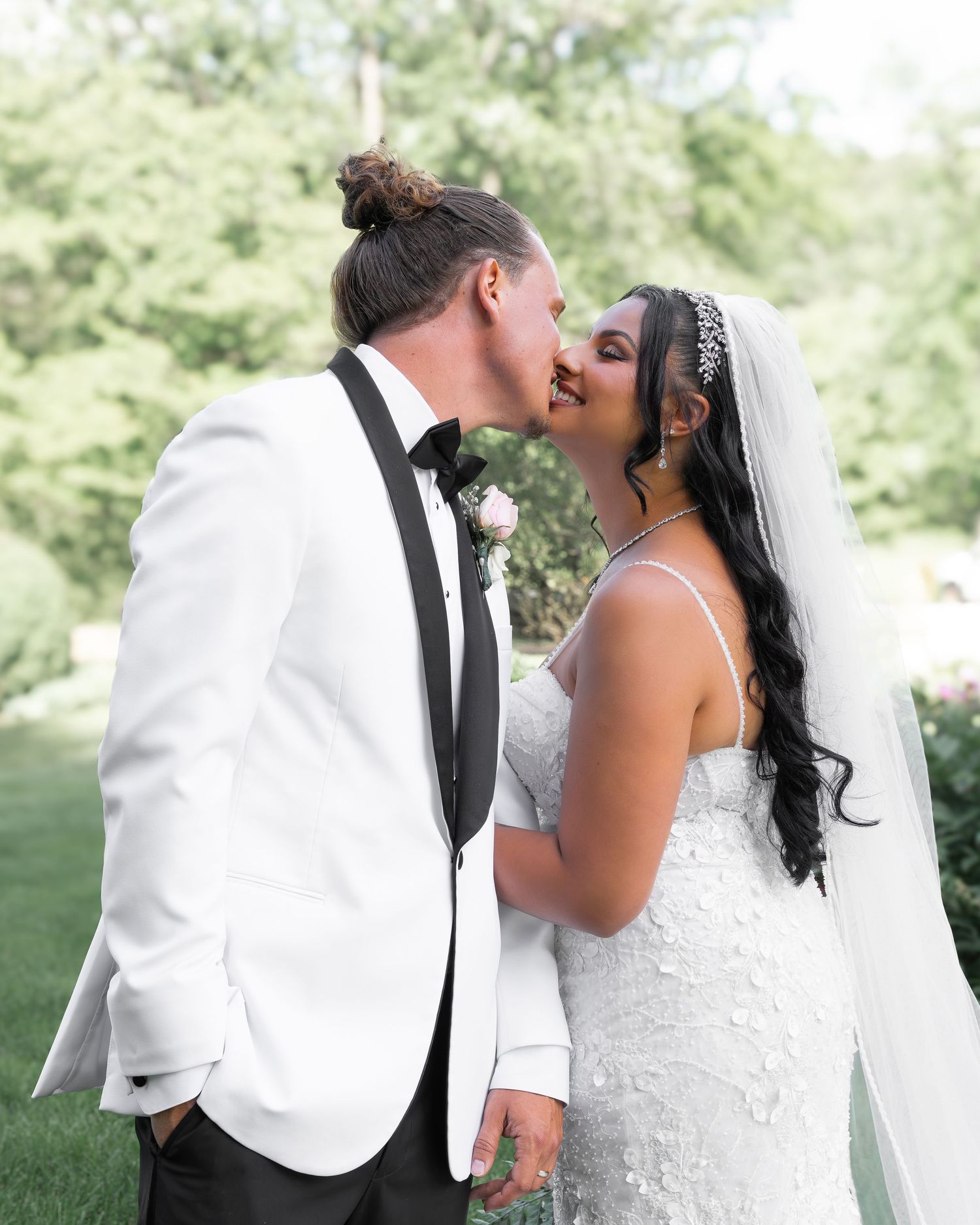 A romantic wedding kiss in a beautiful outdoor garden setting surrounded by soft greenery and natural light.