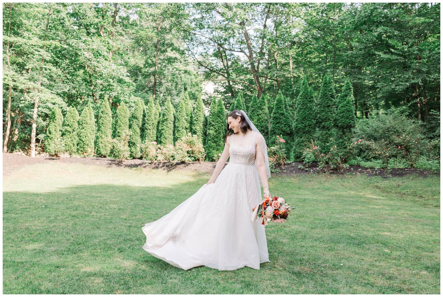 A bride in a flowing white dress twirls in a garden setting while holding a vibrant red bouquet.
