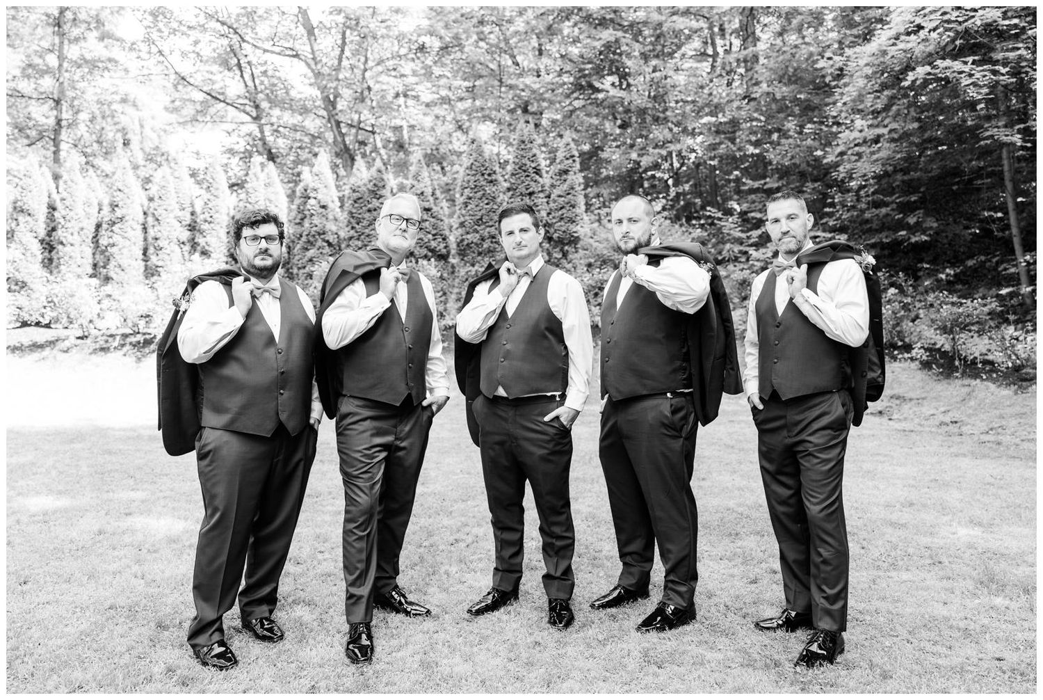 Wedding party in black vests and bowties pose together in a black and white forest setting.